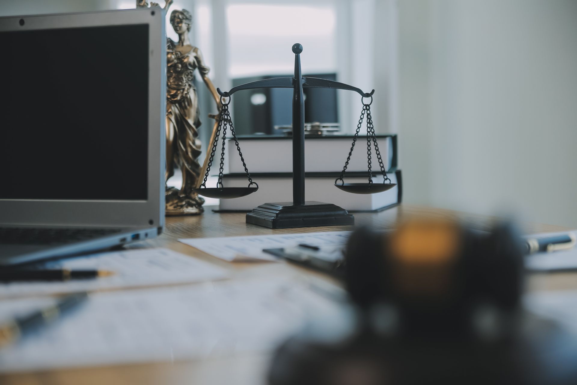 A statue of justice is sitting on a desk next to a laptop and scales of justice.