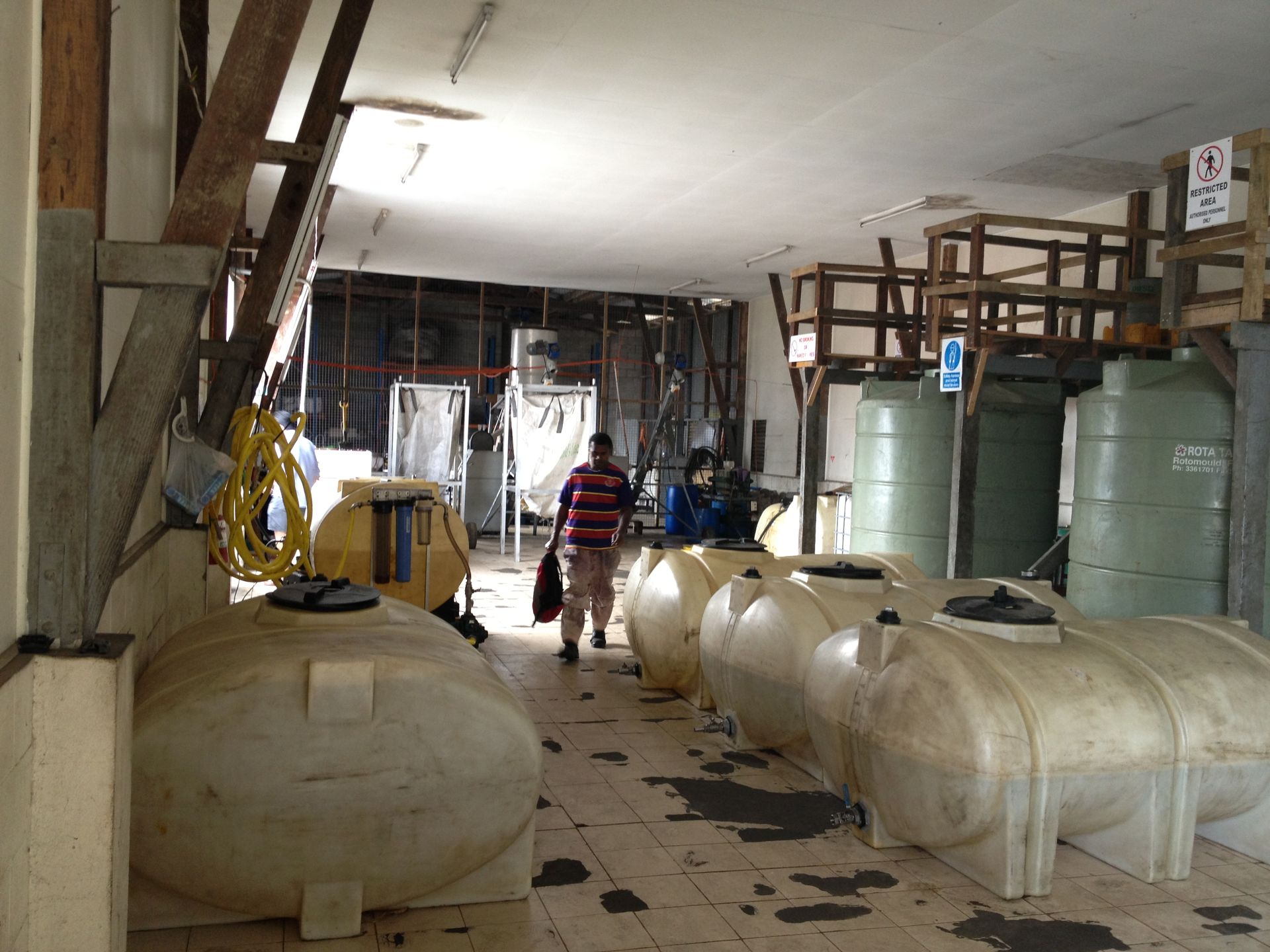 Interior view of a storage area with several large, white plastic tanks. A person walks through the space.