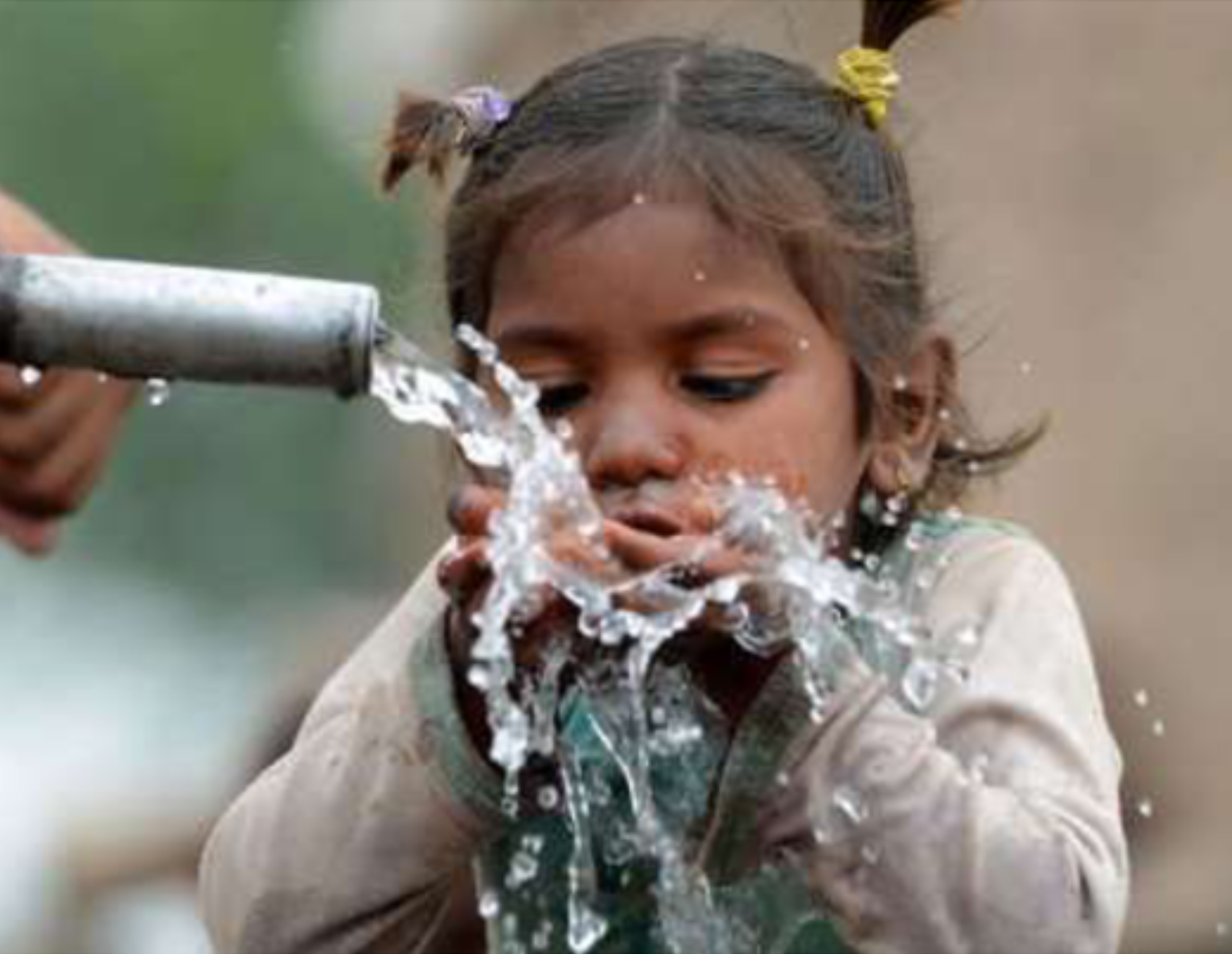 Young girl enjoying drinking from a pipe gushing with clean water