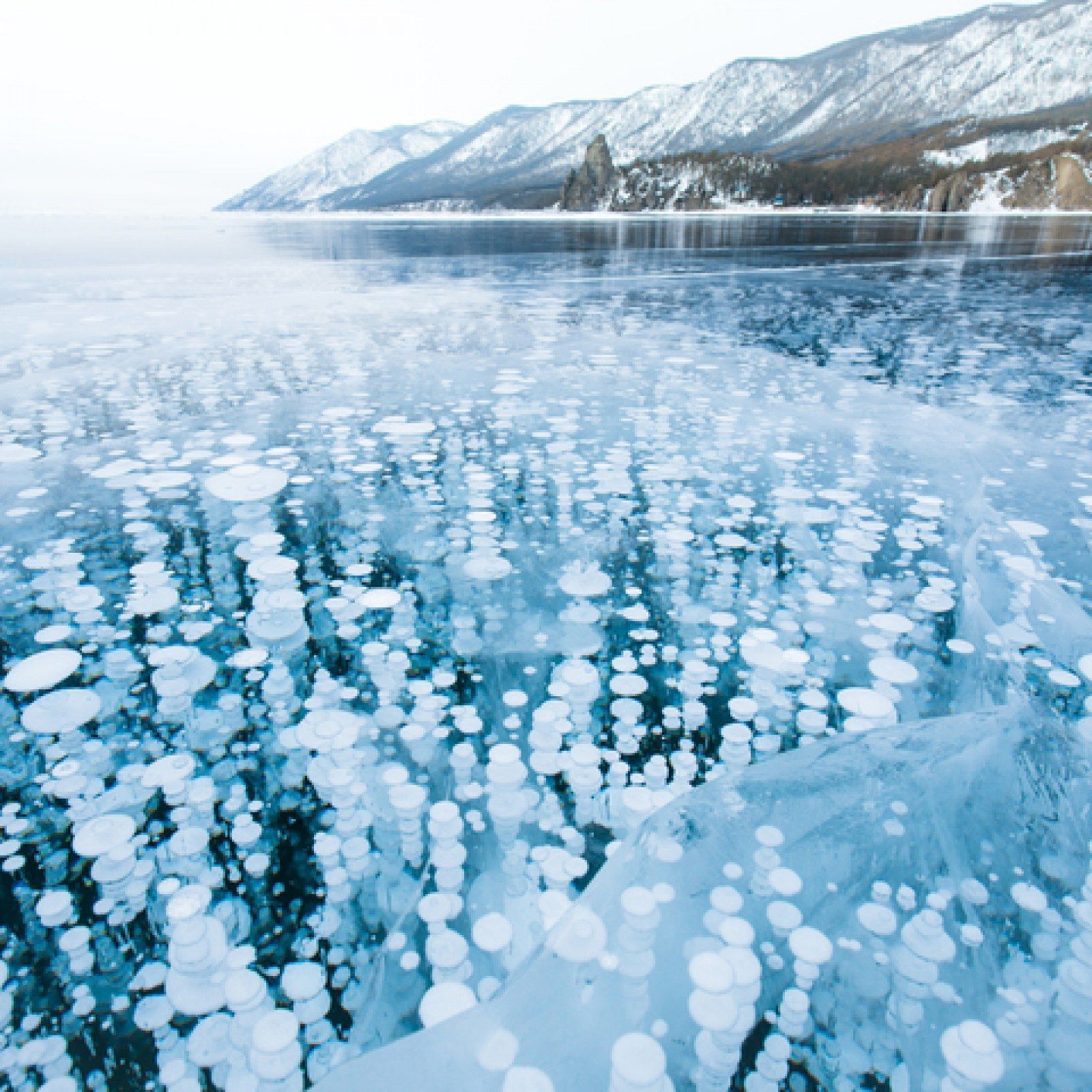 Frozen lake with trapped methane bubbles, mountains in background.