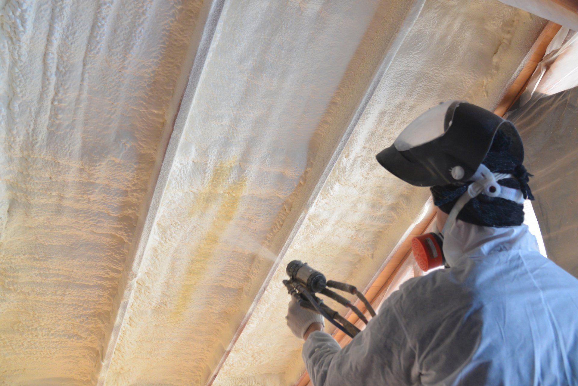 a man wearing a mask spraying foam insulation on a ceiling in Springfield, MA