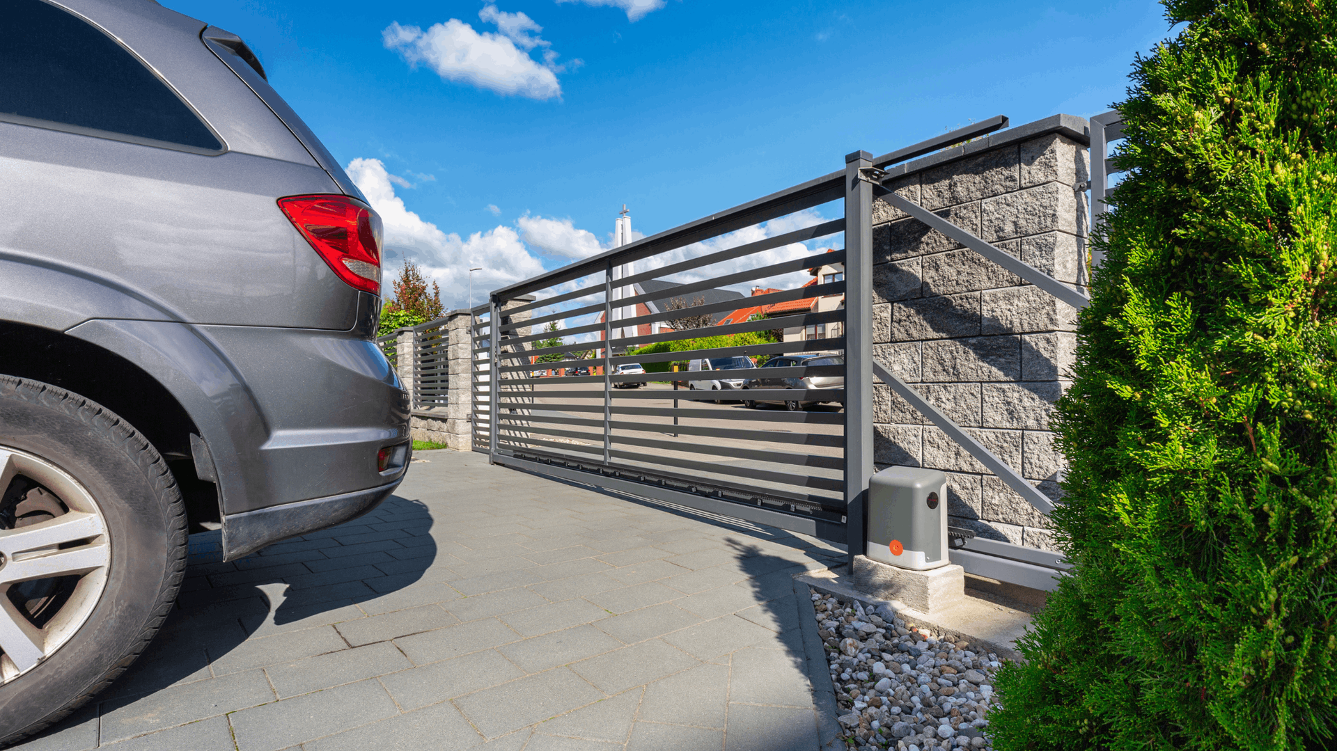 Gray car approaching a modern sliding metal gate set in a stone wall, against a blue sky — Elibon Solutions in Garbutt, QLD