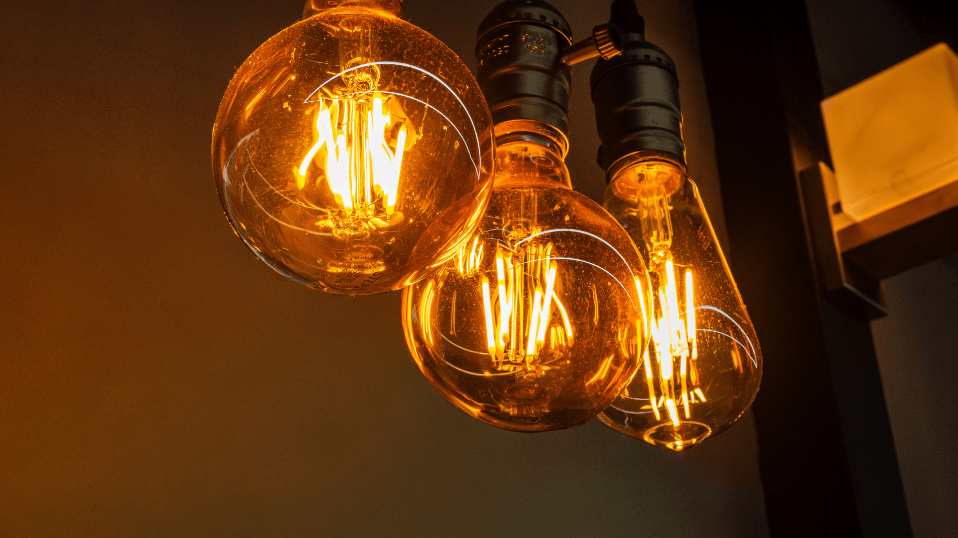 Three illuminated Edison light bulbs hanging. Warm, amber glow against a dark background — Elibon Solutions in Garbutt, QLD
