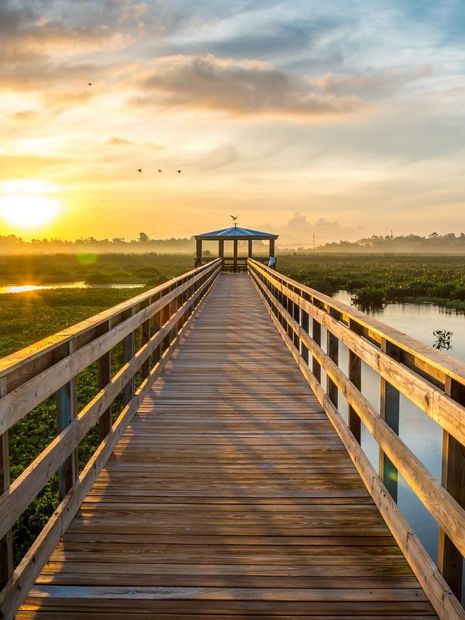 A wooden walkway leading to a gazebo overlooking a body of water at sunset.