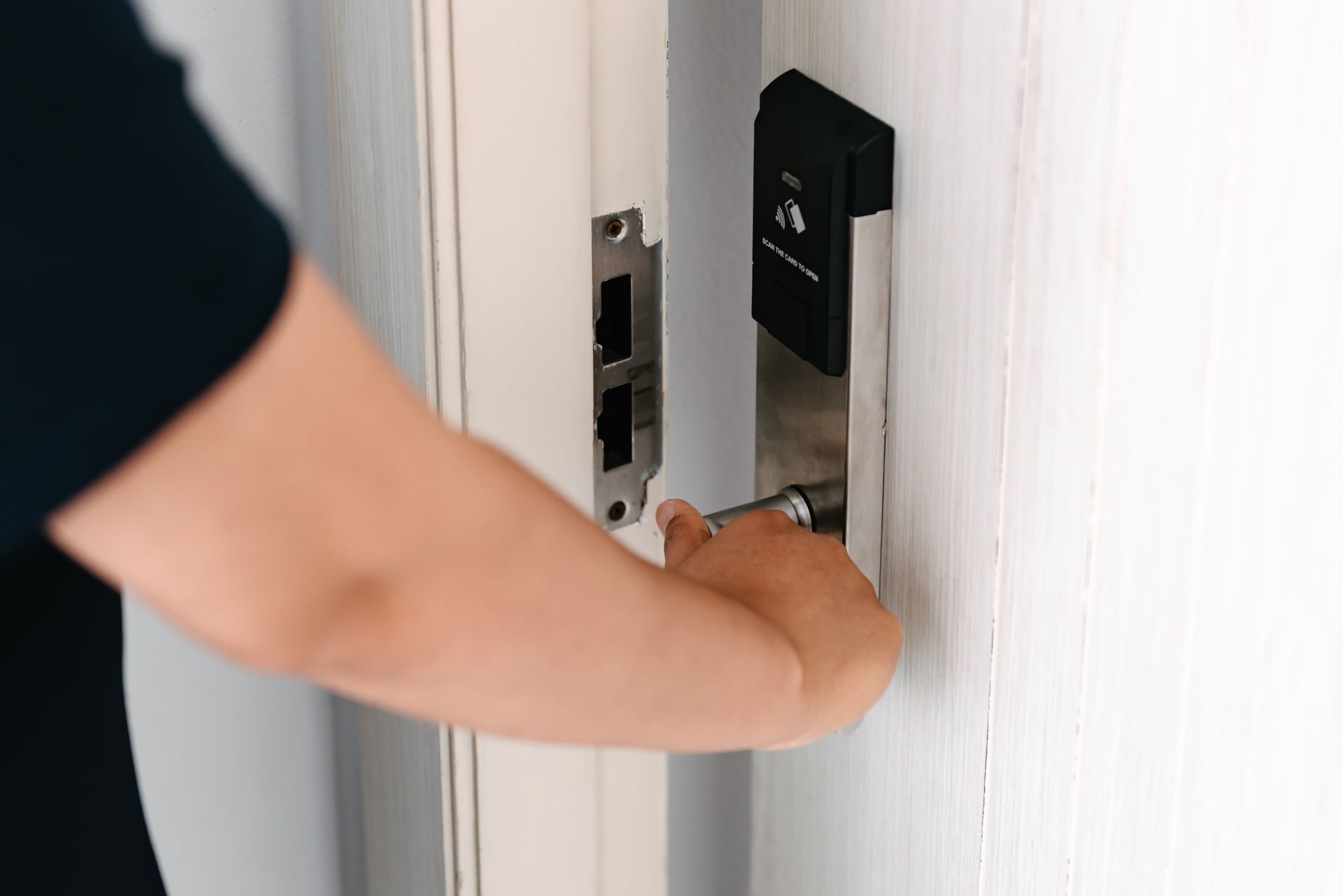 Person unlocking door using electronic lock system with commercial hardware on white door.