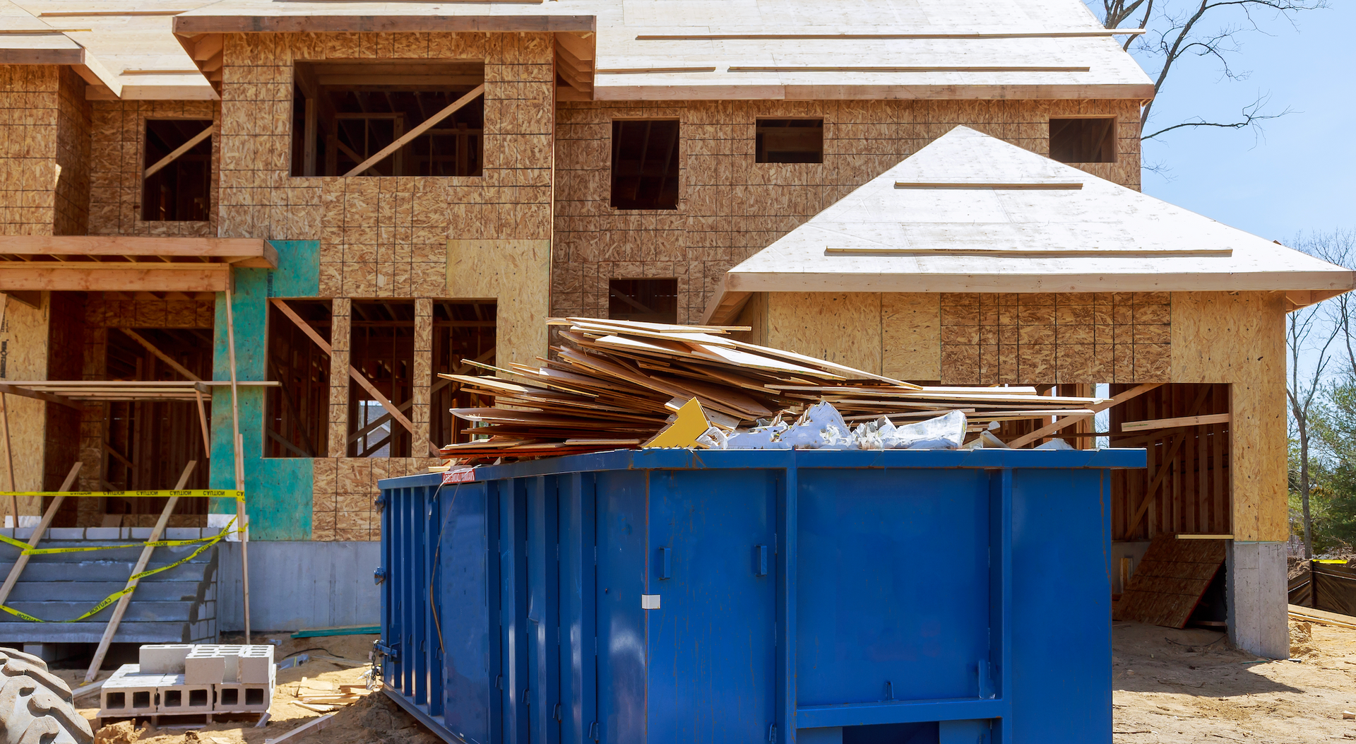 A blue dumpster is sitting in front of a house under construction.