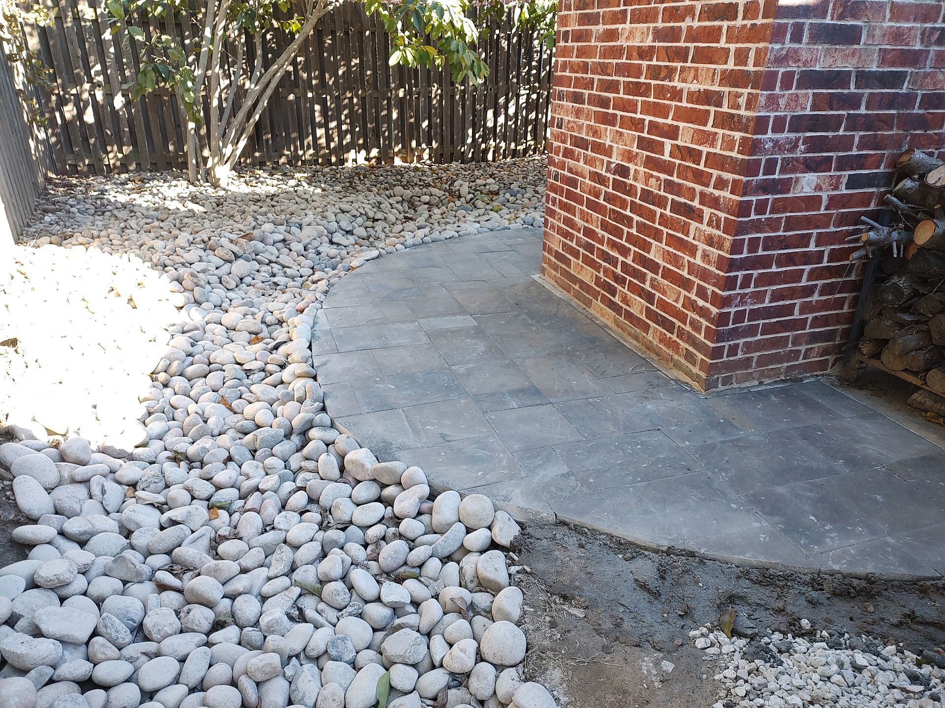 A pathway curves alongside a brick wall and pebble landscaping in an outdoor setting.