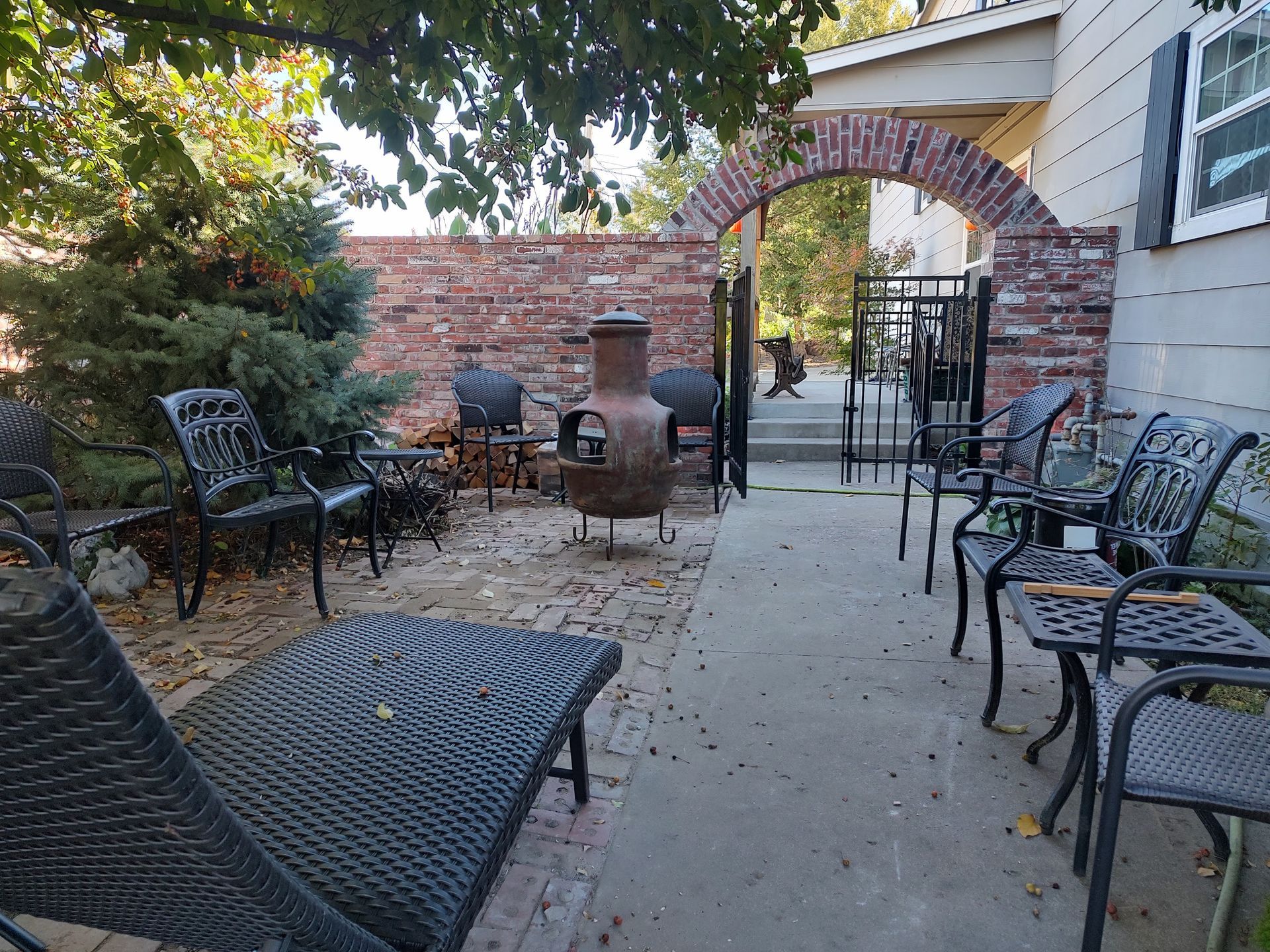 Backyard patio with chairs, brick wall, fire pit, and arched entrance to a path.