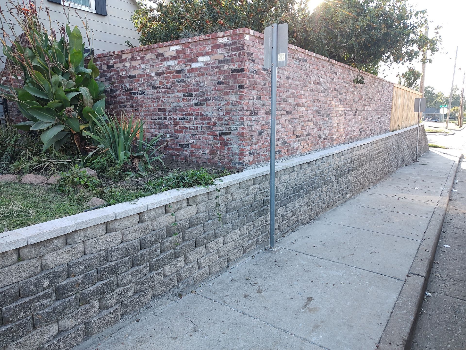 Brick retaining walls alongside a sidewalk, with a brick wall and vegetation above.