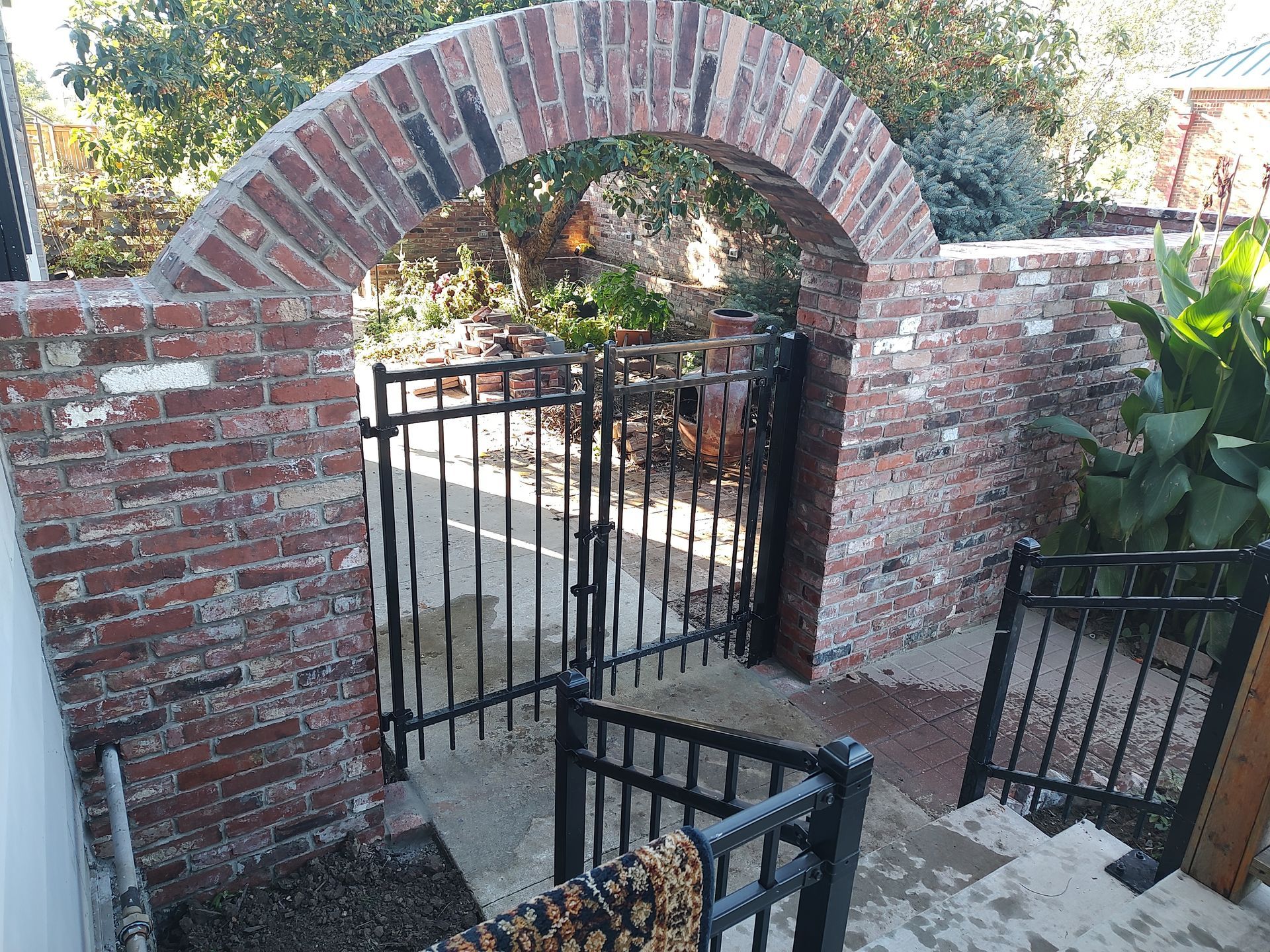 Brick archway over a black wrought iron gate leading to a garden, with steps down.