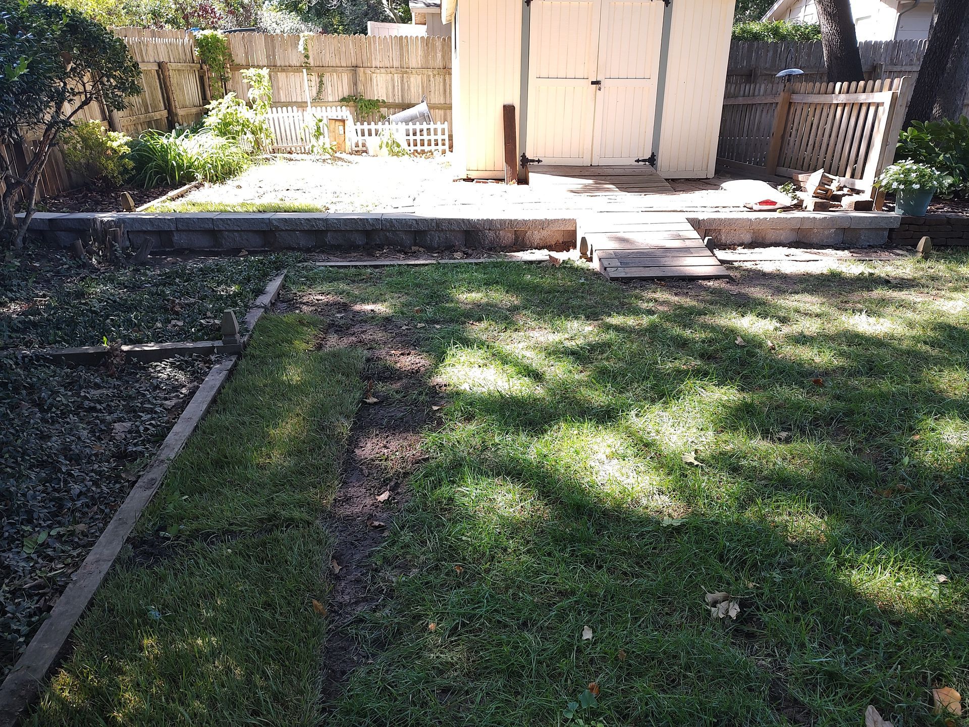 Backyard with a shed, retaining wall, and patchy grass.