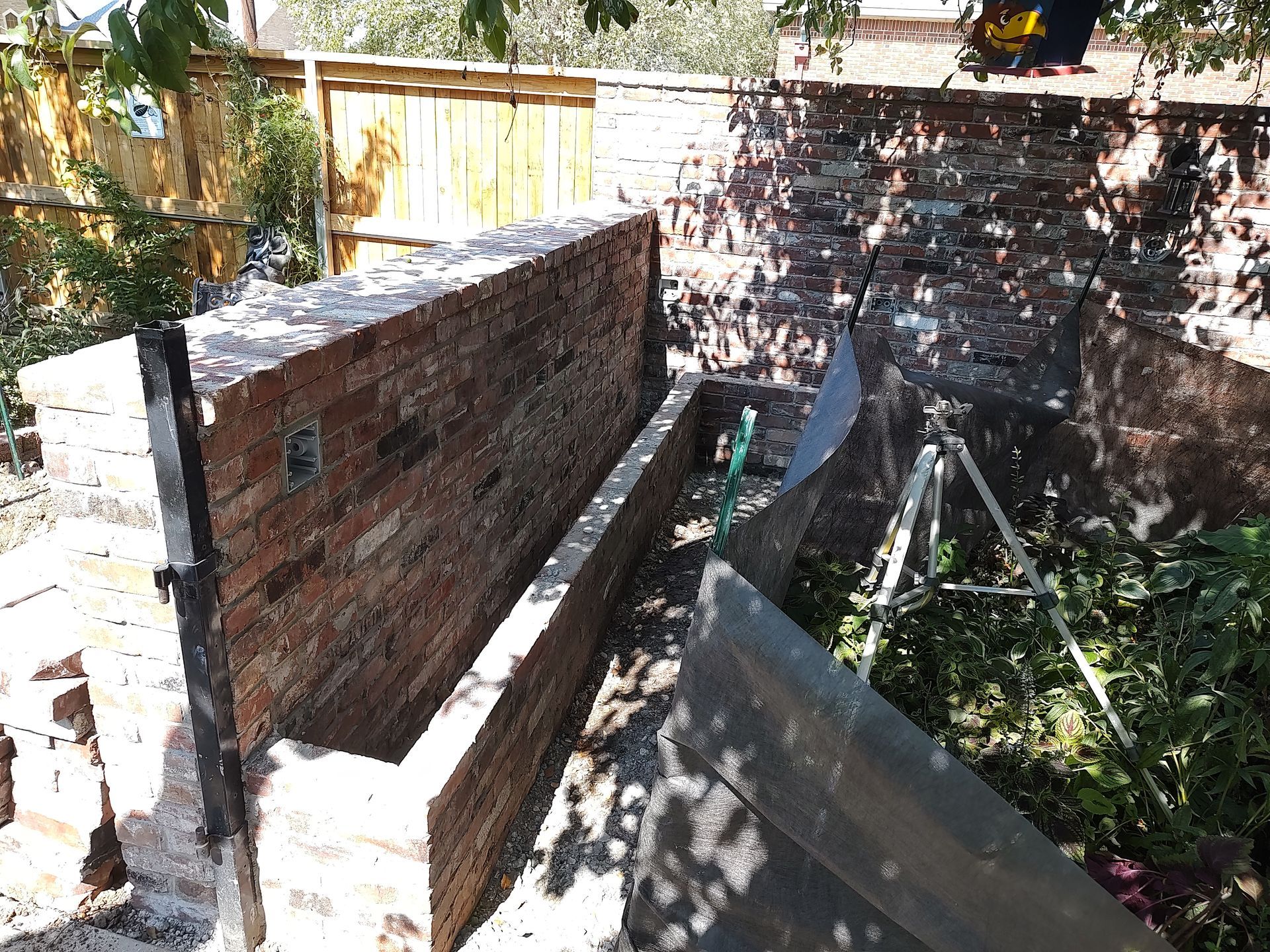Brick wall construction in a garden setting, with wood fence and galvanized sheeting.