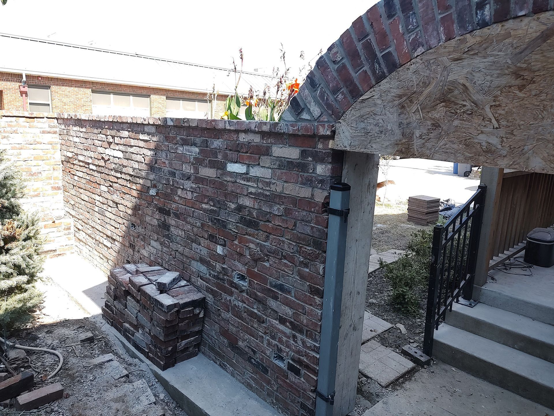 Brick wall with arched doorway, outdoor setting, concrete steps, and a black metal railing.