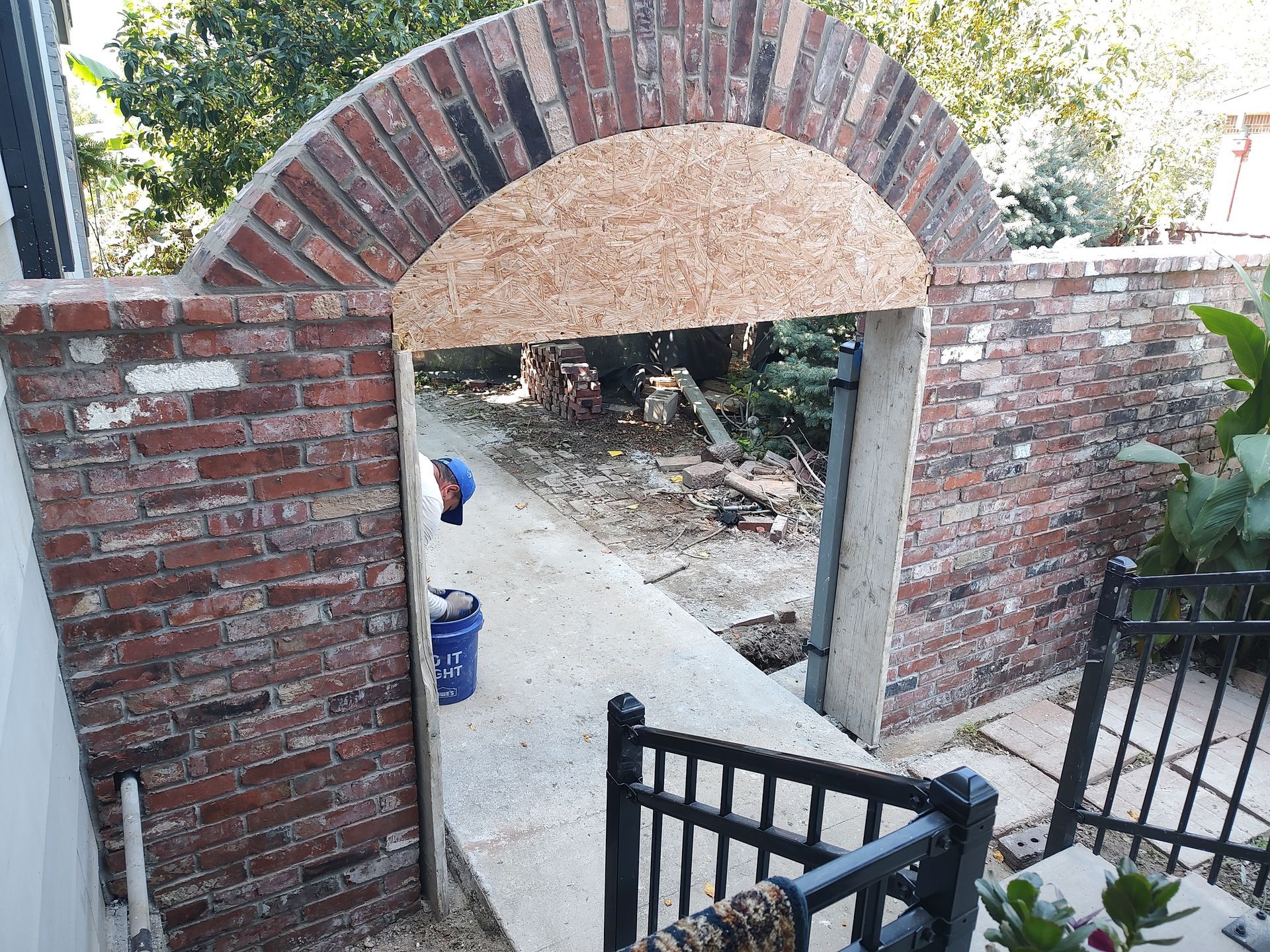 Brick archway in progress; opening to pathway; bucket and tools present.