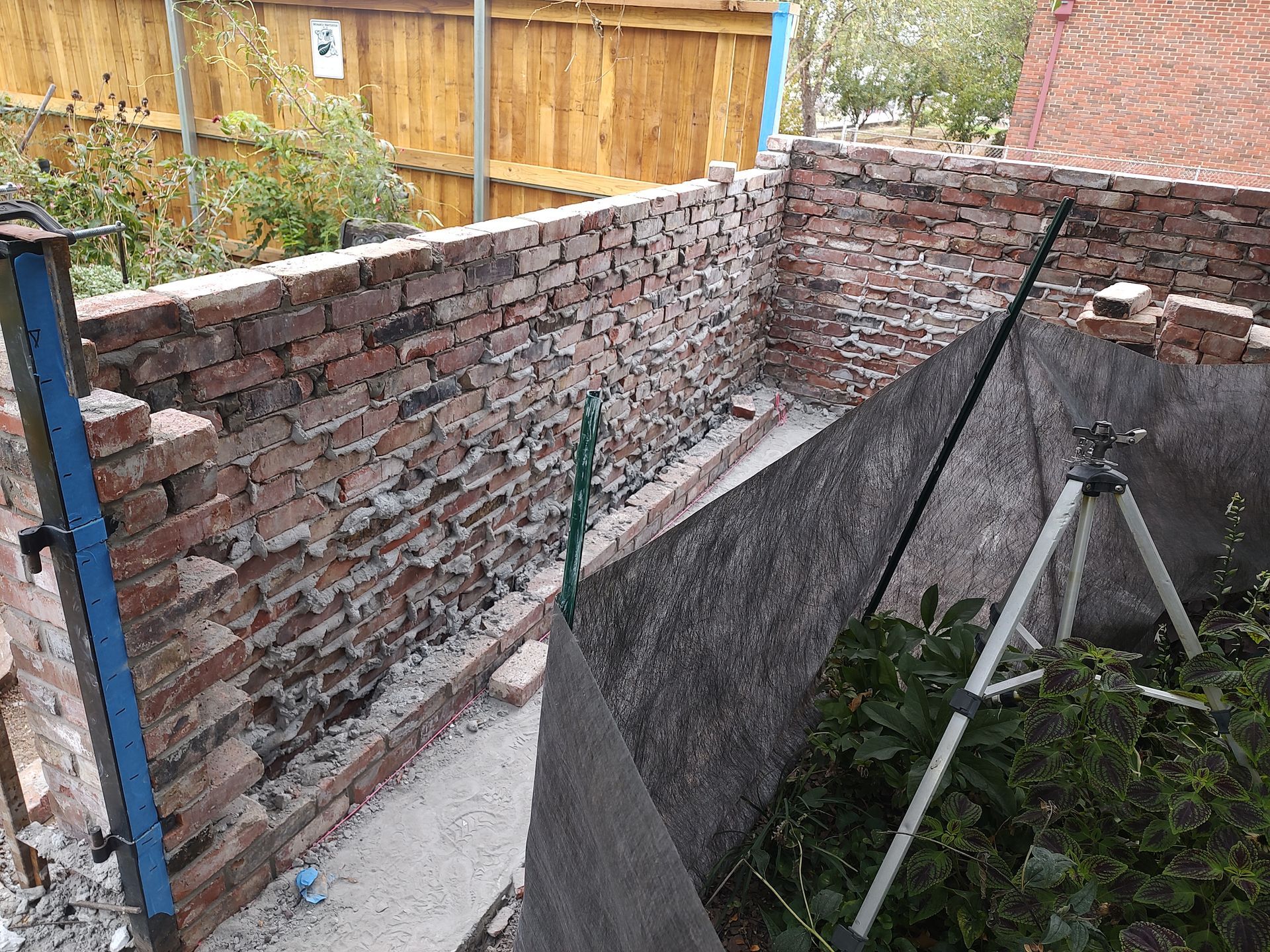 Brick wall being built; level, tripod, and green hose present.