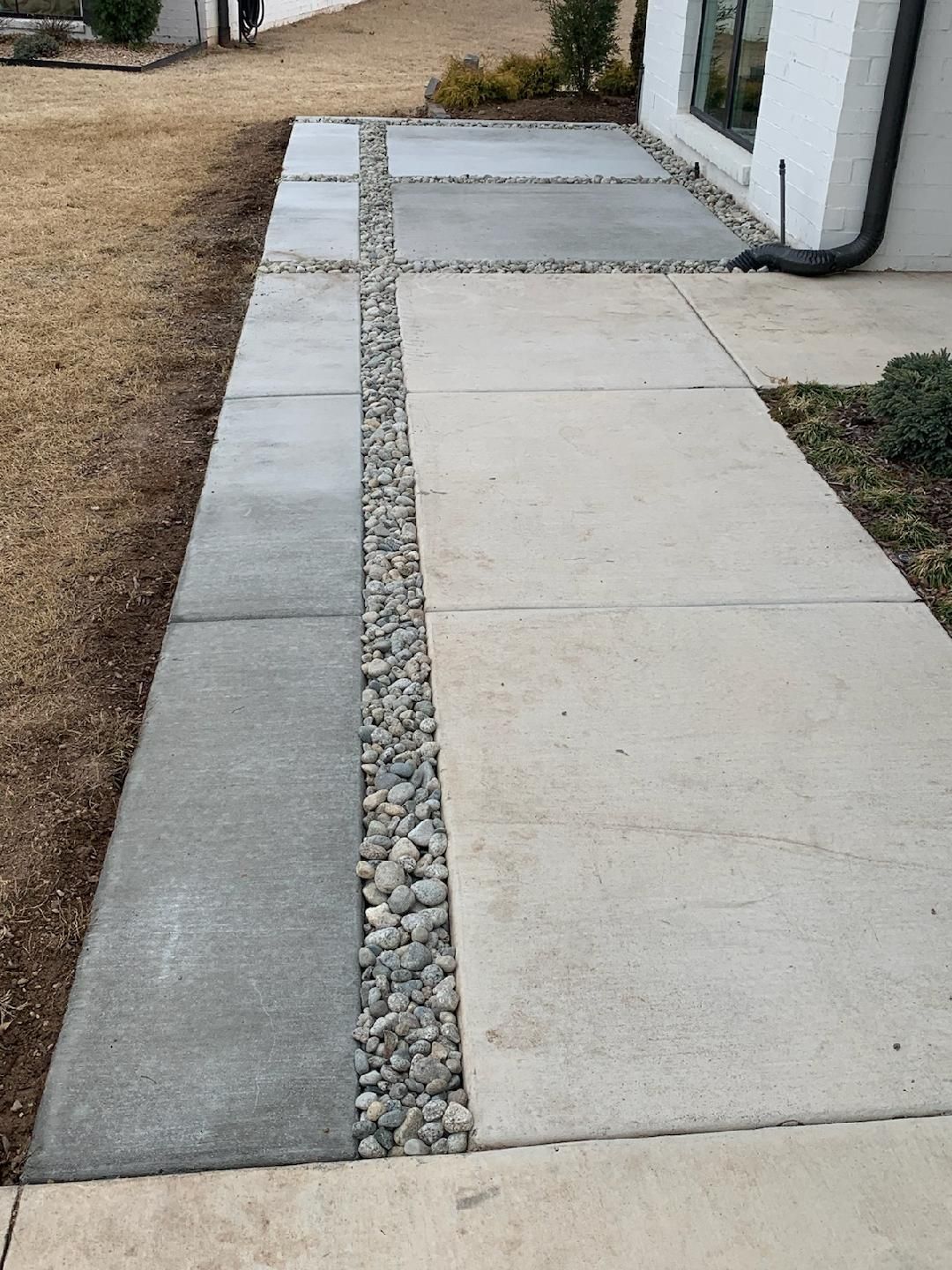 Concrete walkway with gray and beige squares, a center strip of gravel, and a white building.