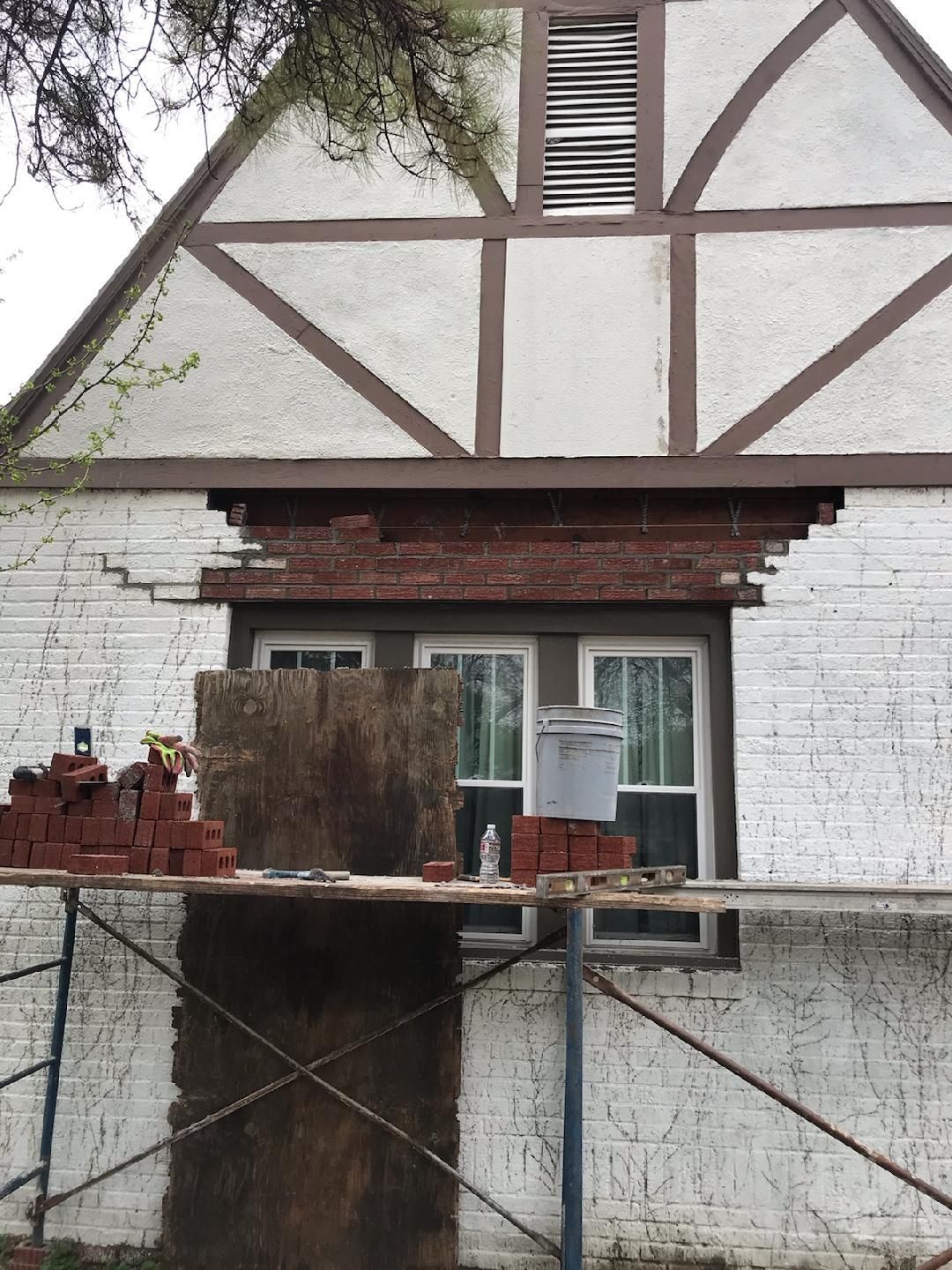House exterior with brickwork repair underway; scaffolding, window, and brown and white facade visible.