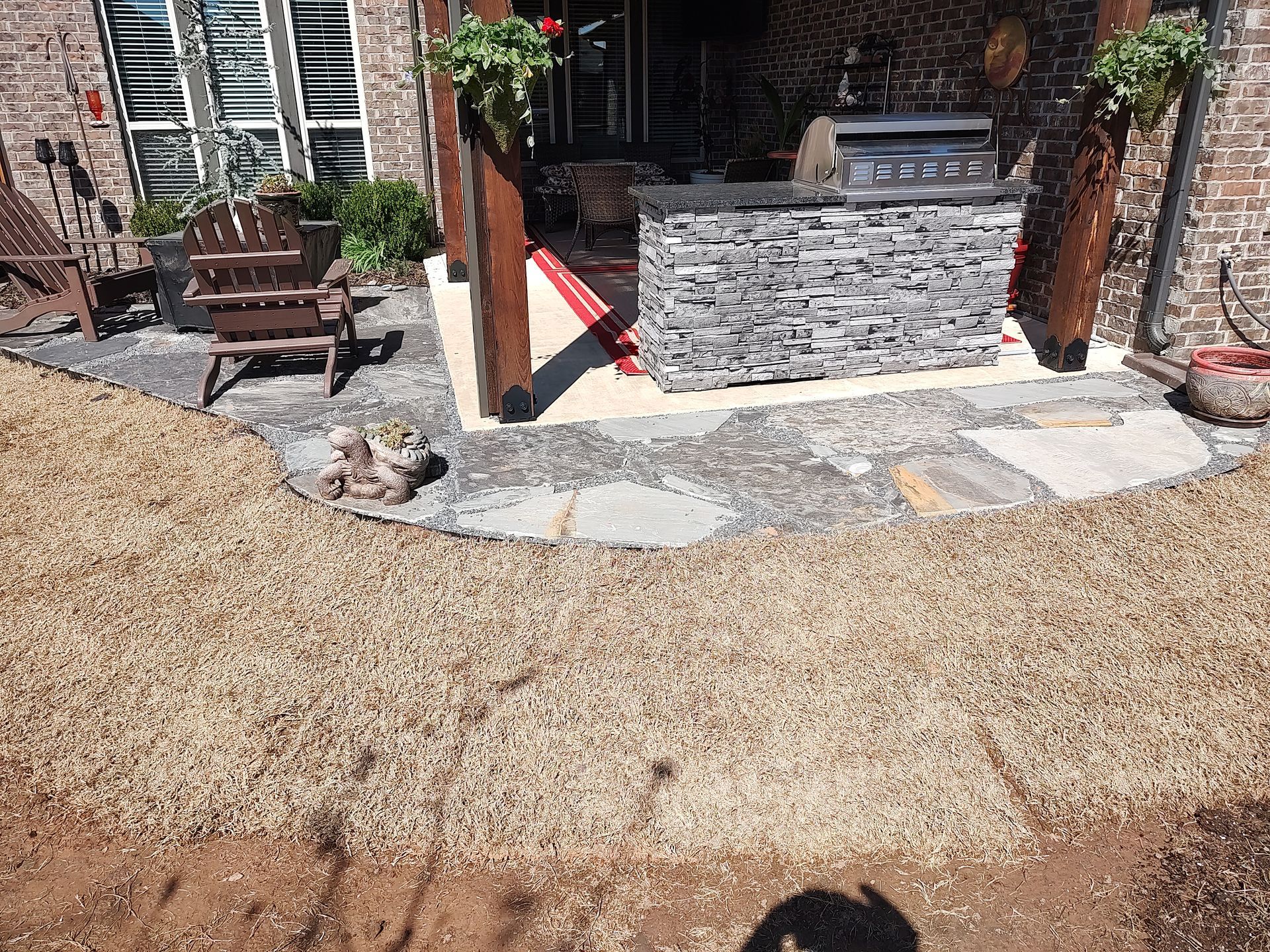 Outdoor patio with a stone-covered grill, gravel pathway, and a wooden chair.