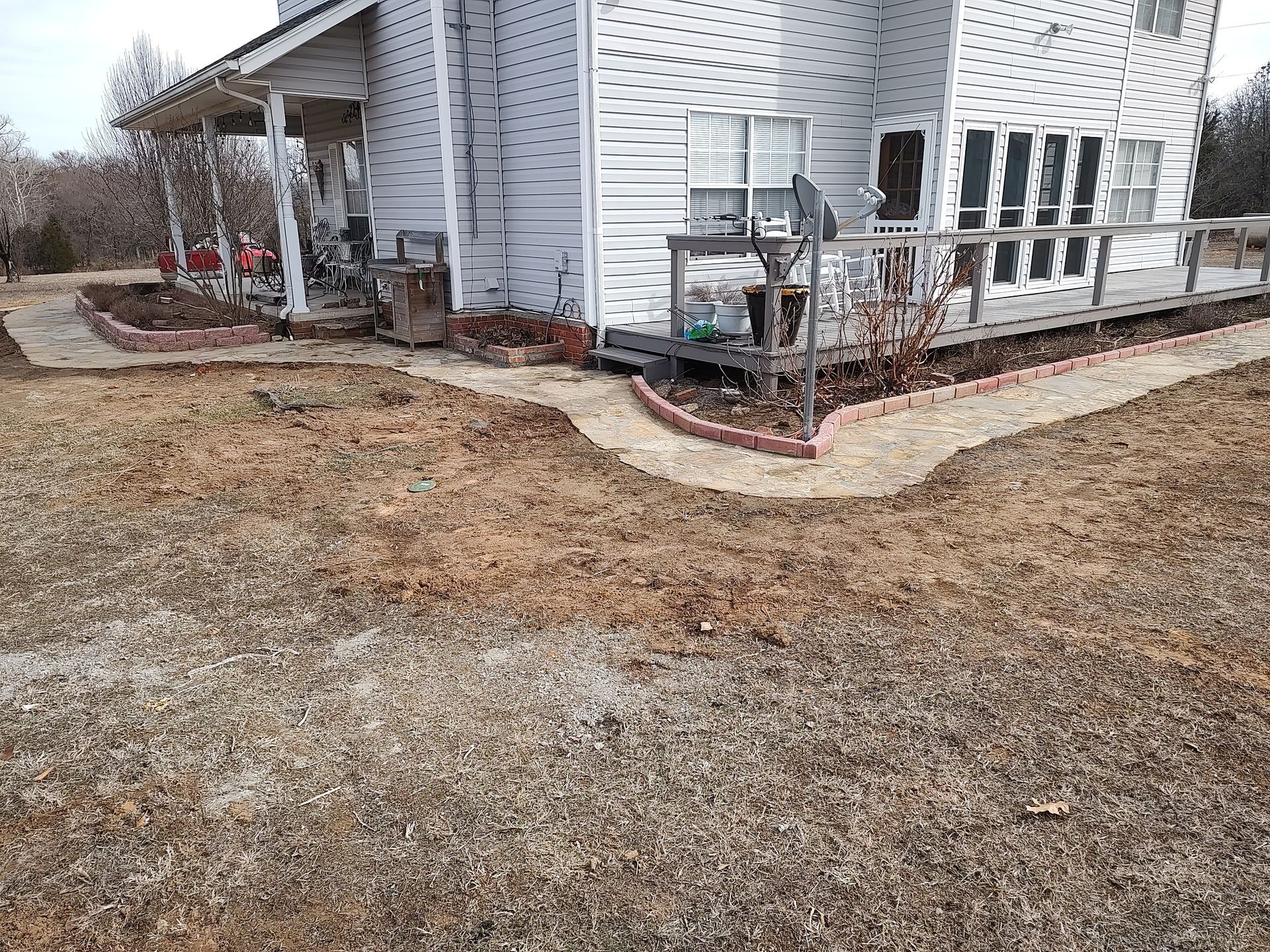 A two-story white house with a porch and a dirt yard with a brick-lined path.