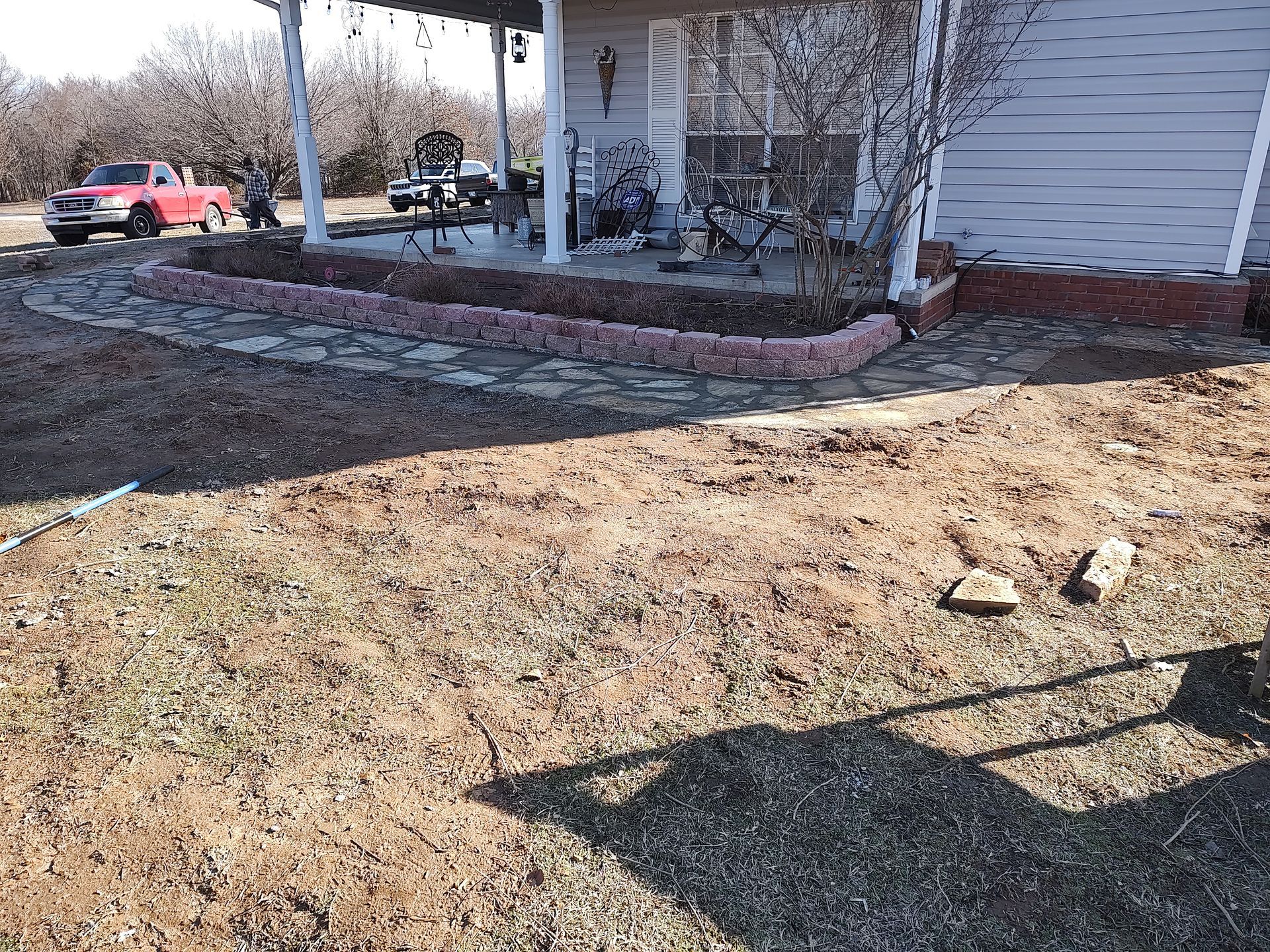 A house exterior with a red truck, porch, and a flower bed edged with red brick.