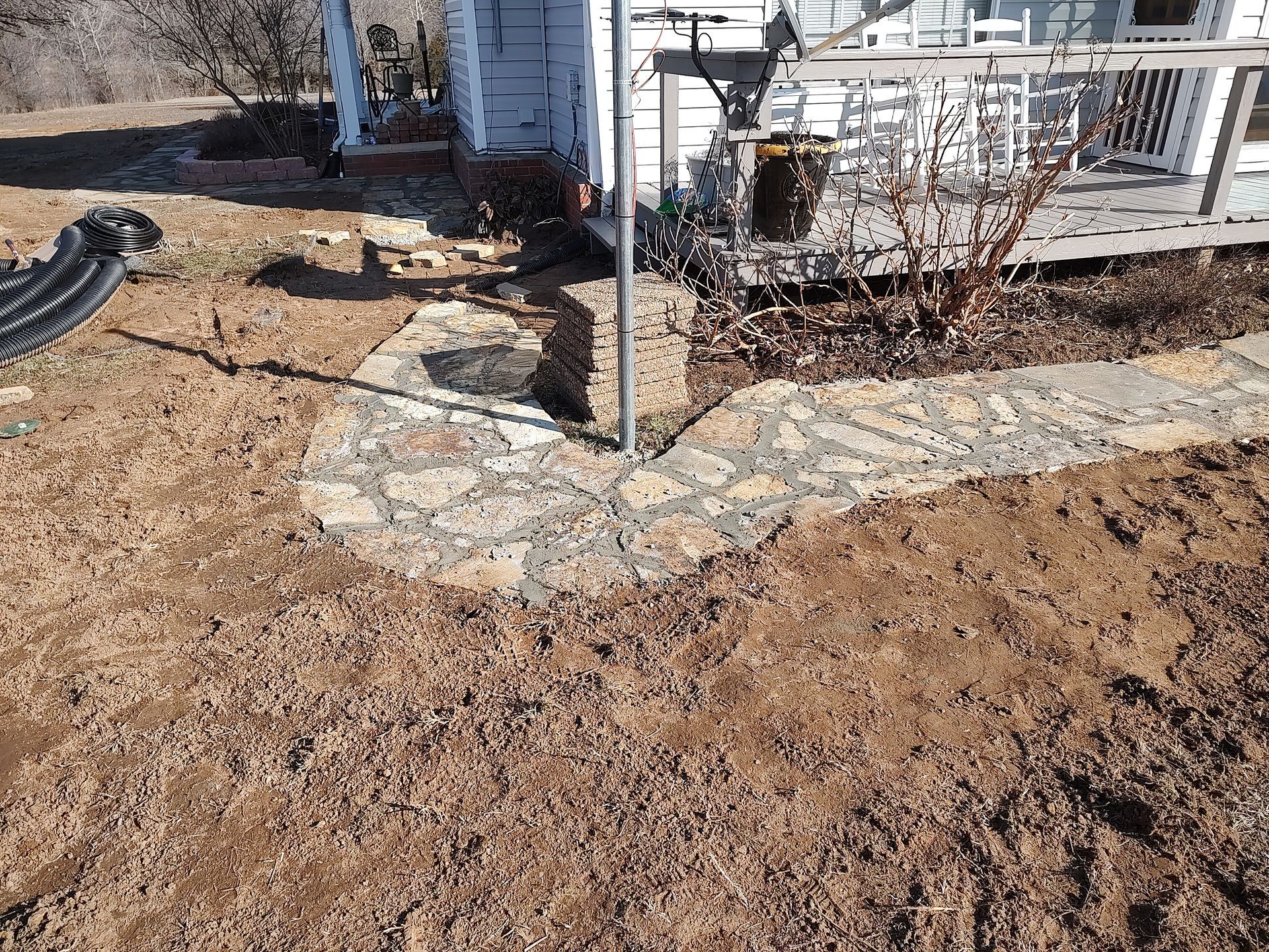 Stone path curving towards a house, surrounded by dirt and sparse vegetation.
