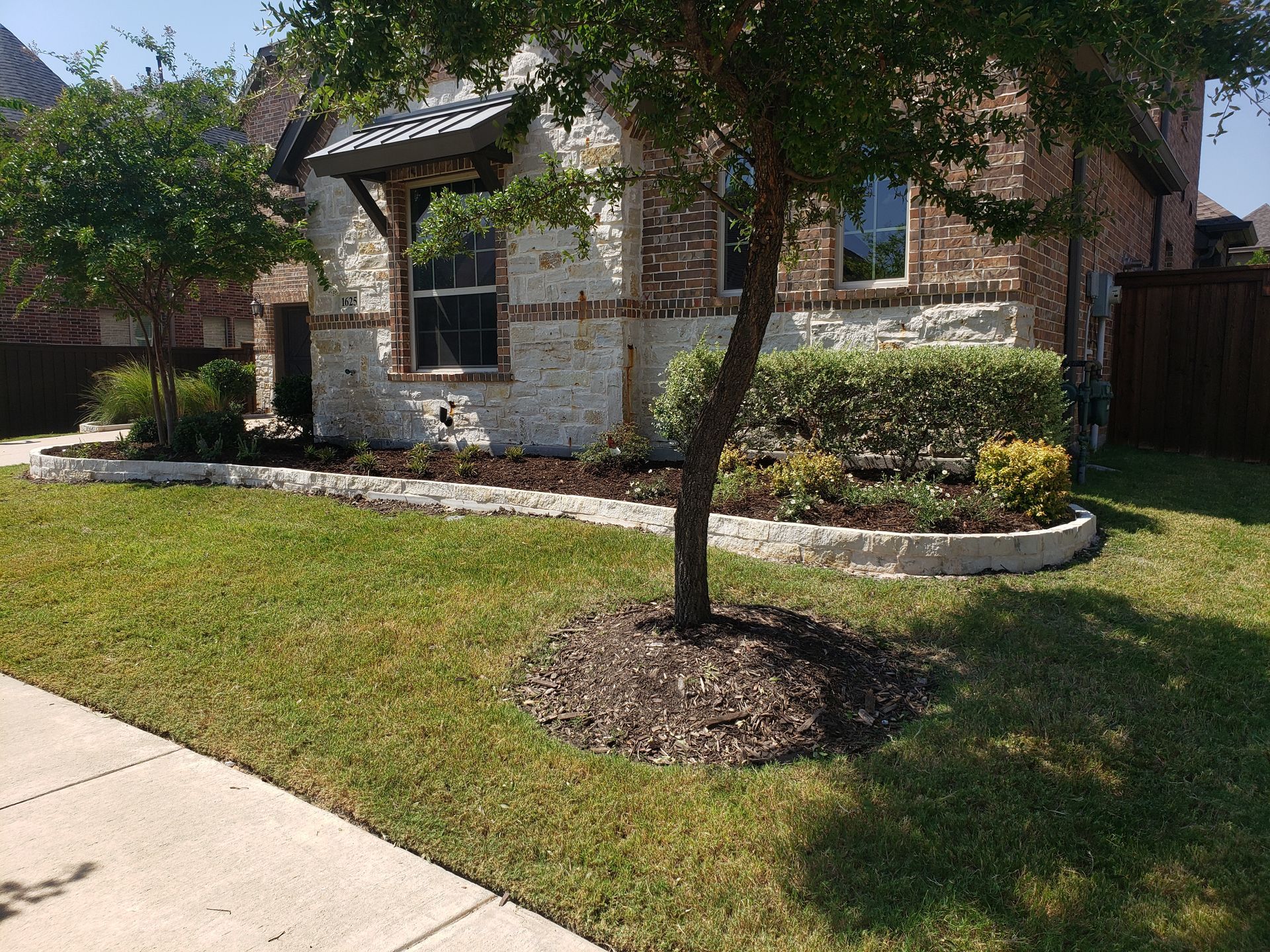 House exterior with stone and brick facade, landscaping, and a tree in front.