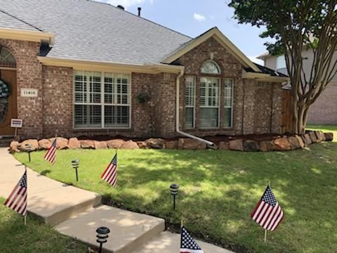 House exterior with brick facade, green lawn, American flags, and a tree.