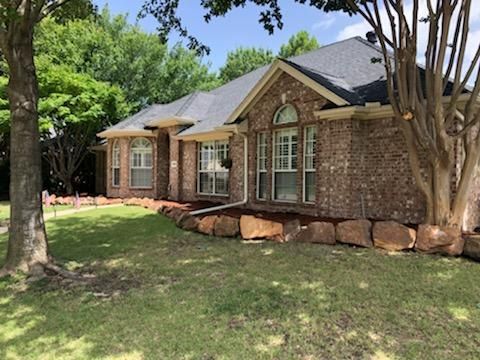 Brick house with arched windows, dark roof, and rock border on a sunny day.