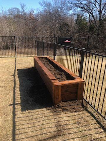 Wooden raised garden bed, filled with soil, inside a fenced yard.