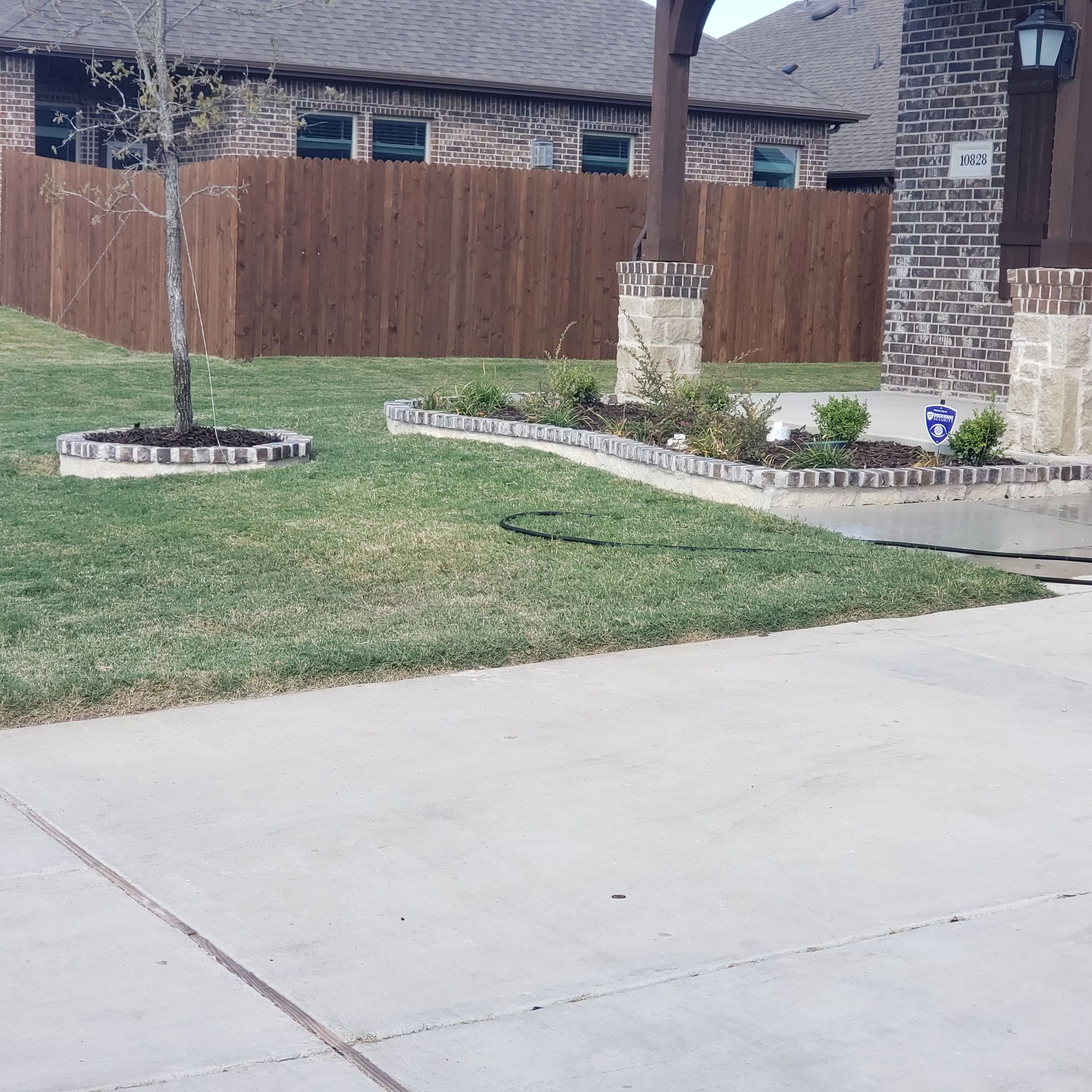 A house exterior with a manicured lawn, landscaping, a wooden fence, and concrete driveway.