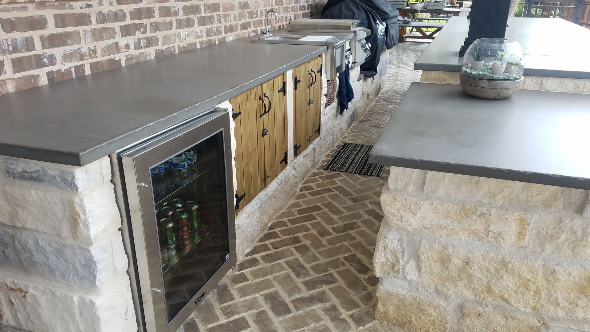 Outdoor kitchen with stone and brick, concrete countertops, and a beverage cooler.