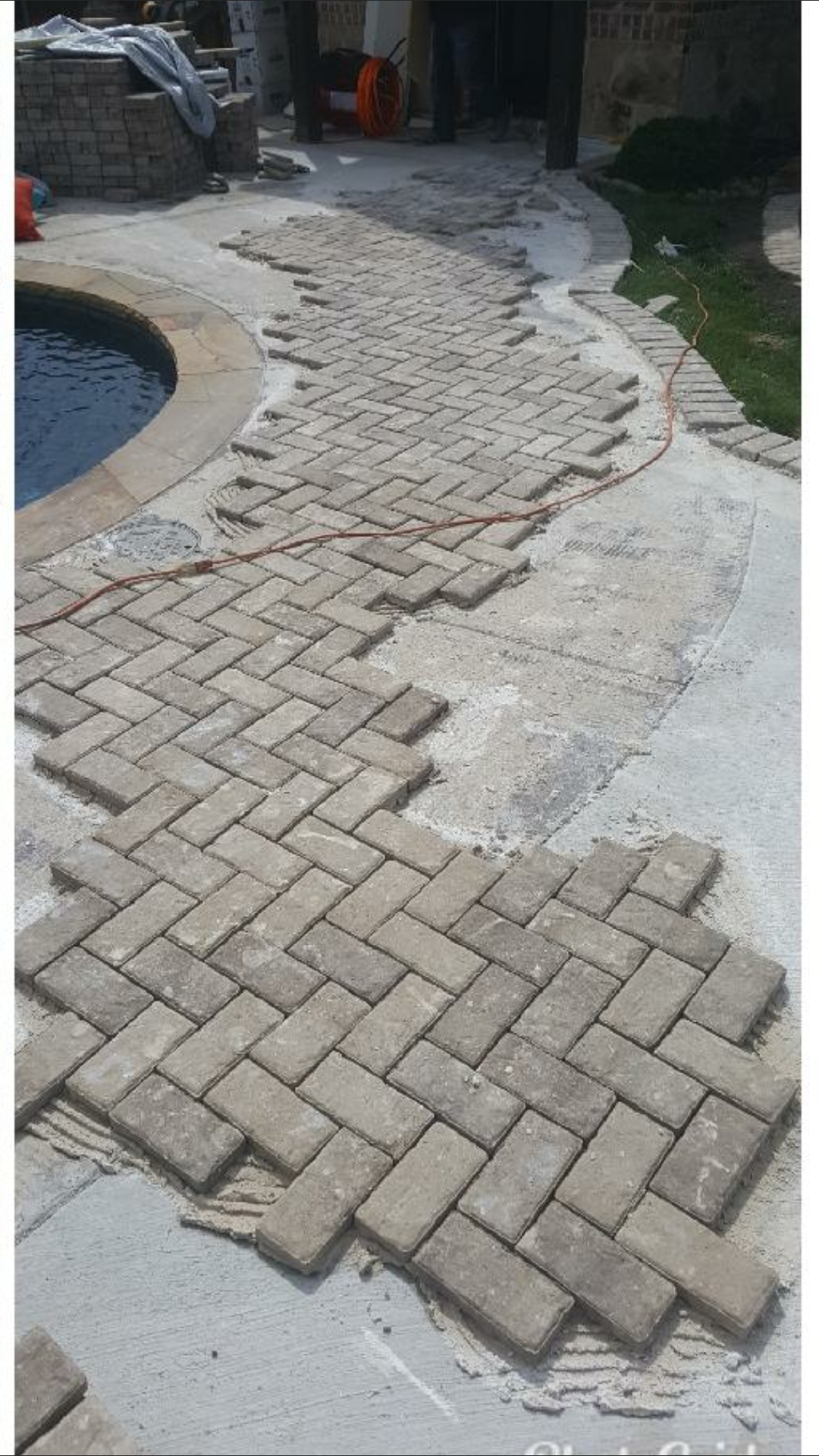Path of brick pavers being laid near a pool.