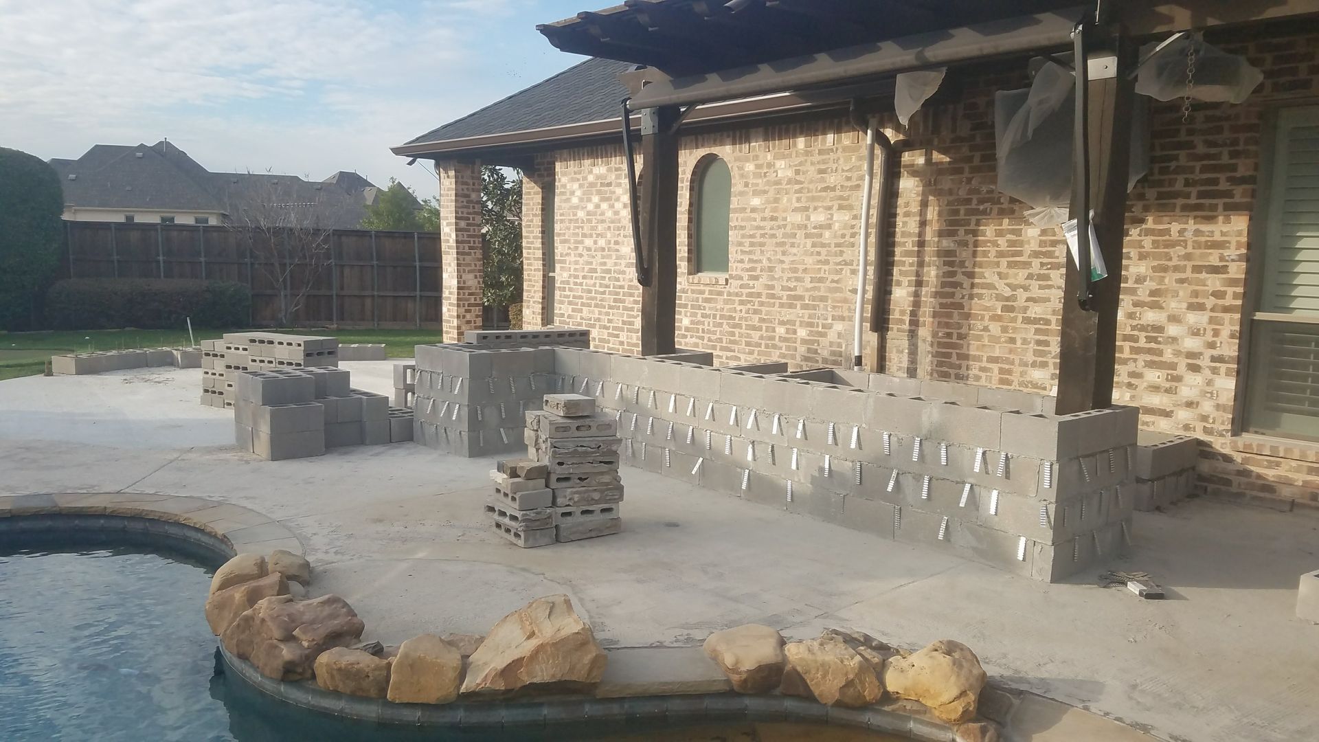 Backyard with pool and construction, featuring brick building, concrete blocks, and sandy surface.