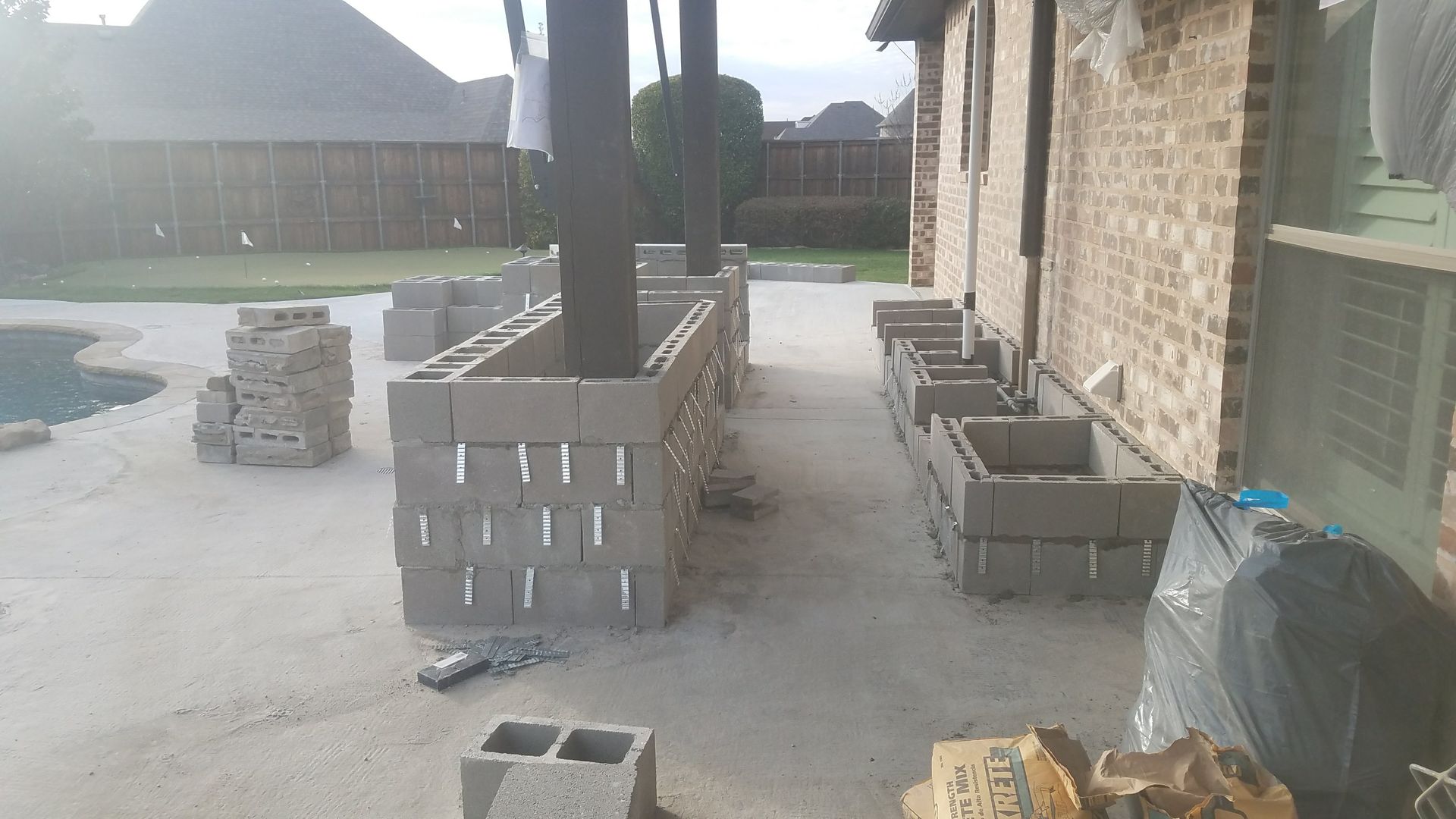 Concrete block construction on a patio near a pool. Grey blocks stacked to form walls under a covered structure.
