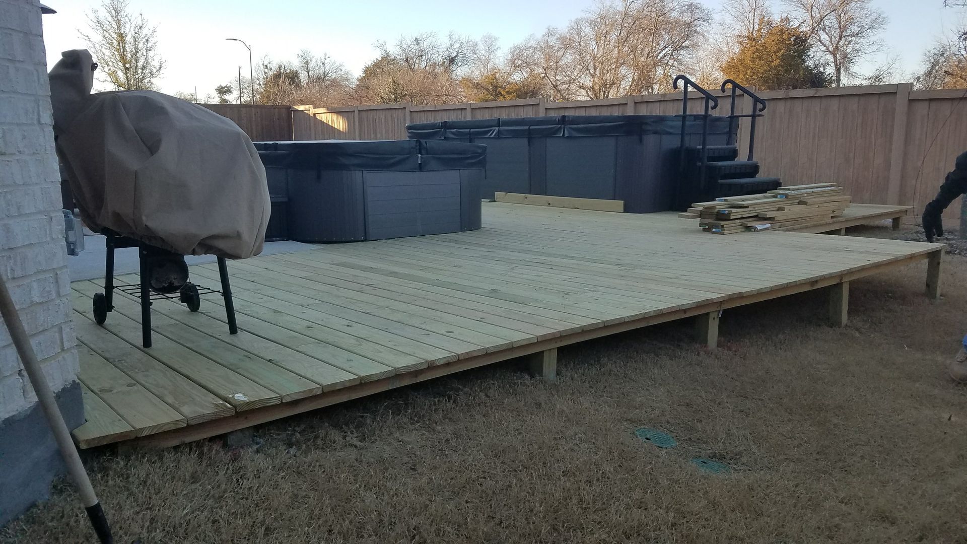 Wooden deck with covered hot tubs, grill, and fenced backyard.