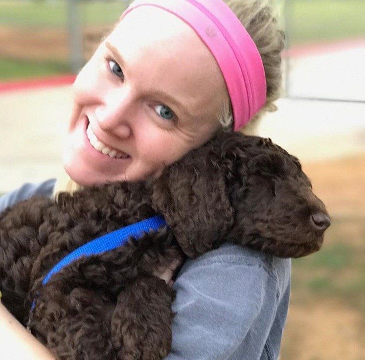 Woman holding a small brown dog, both smiling. The woman wears a pink headband and blue shirt.