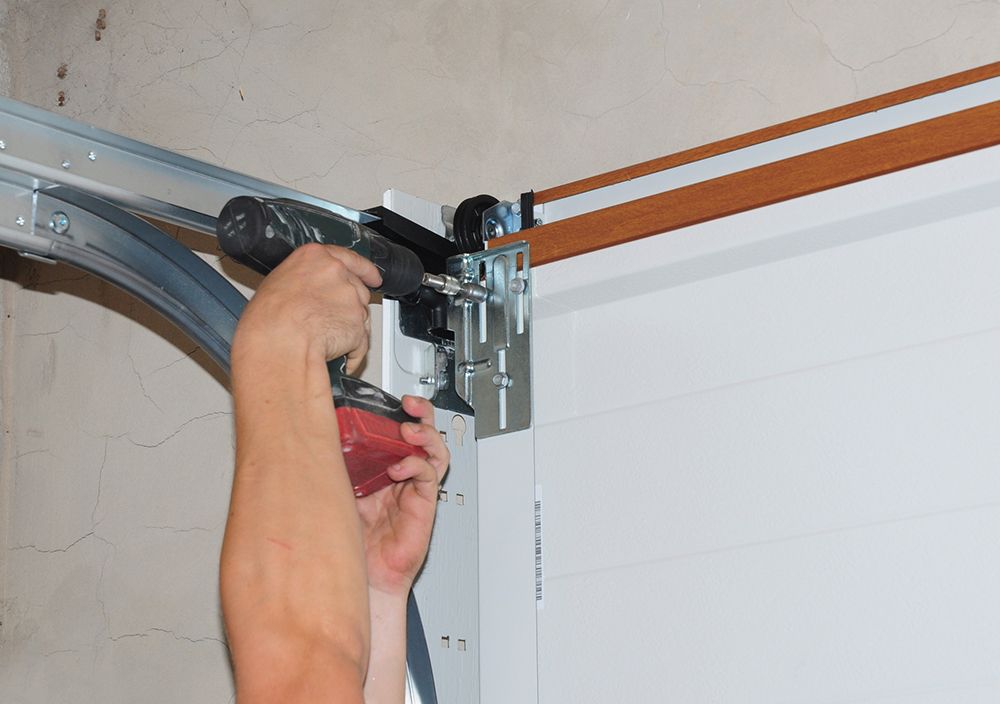 A man is fixing a garage door with a drill.