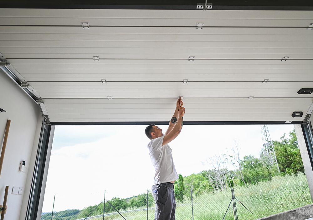 A man is fixing a garage door with a screwdriver.
