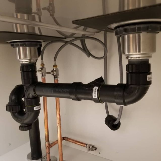 Hand using pliers on pipe near a water heater in a utility room.