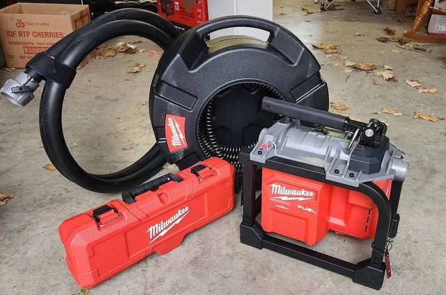 Person using an orange drain snake to unclog a kitchen sink.