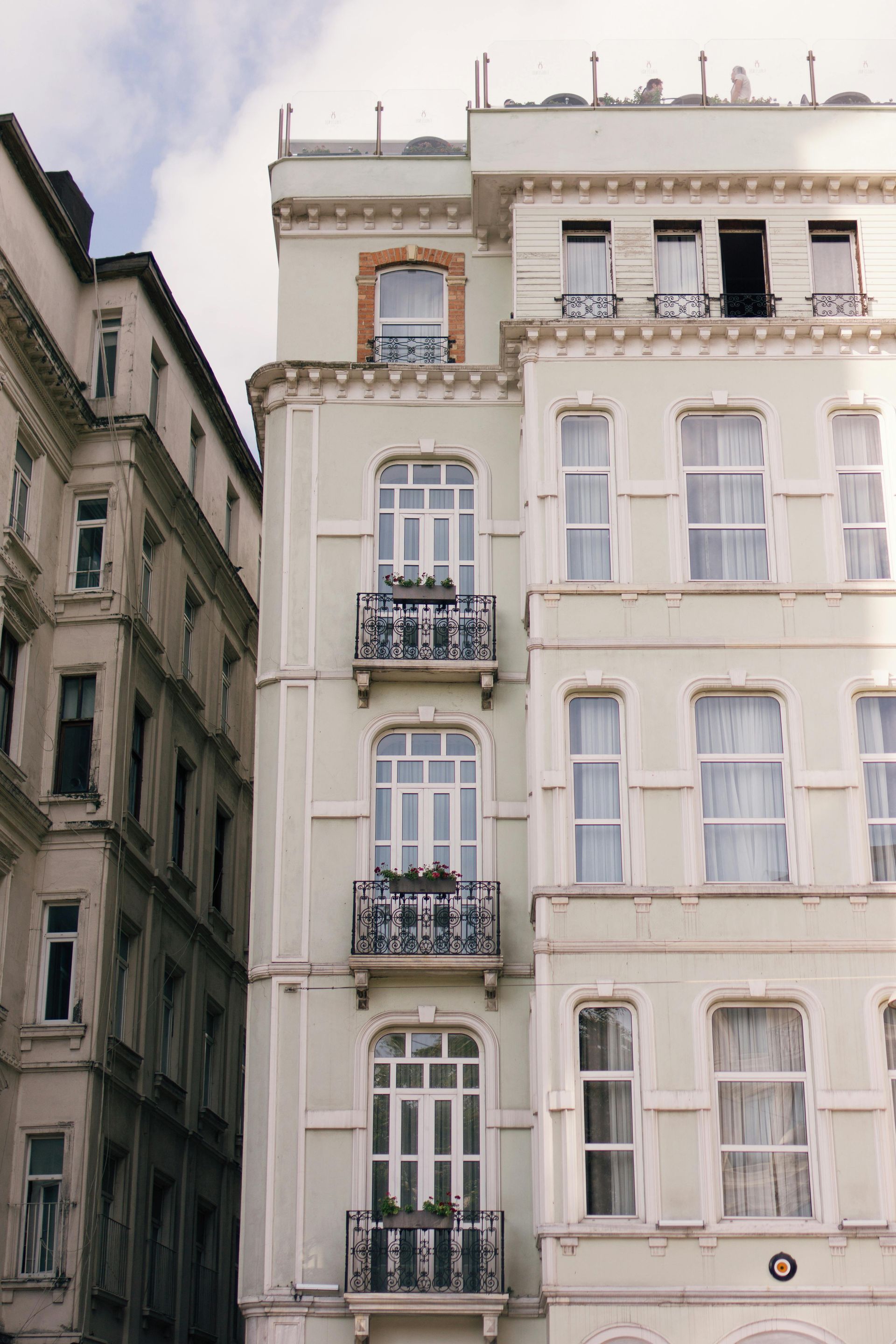 Mehrgeschossige Wohnhäuser, hellgrüne Fassade mit weißen Zierelementen, einige Balkone, sonniger Tag.
