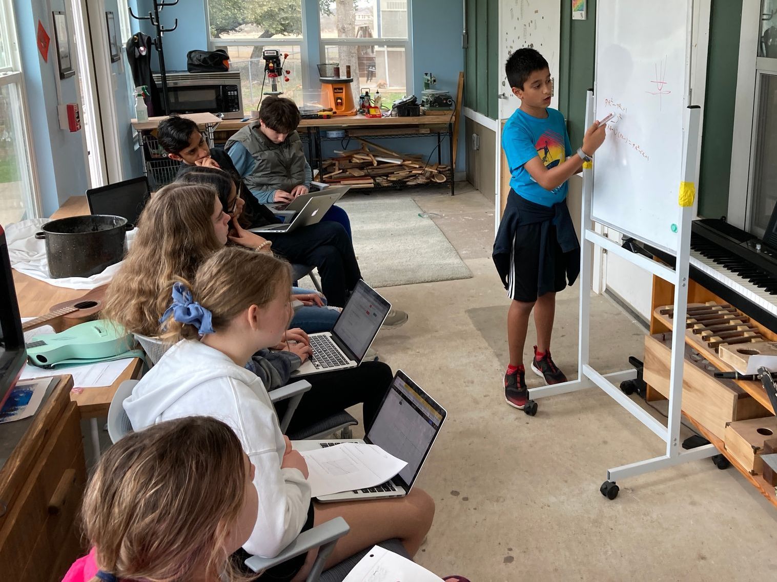 A Montessori student in a blue shirt is writing on a white board