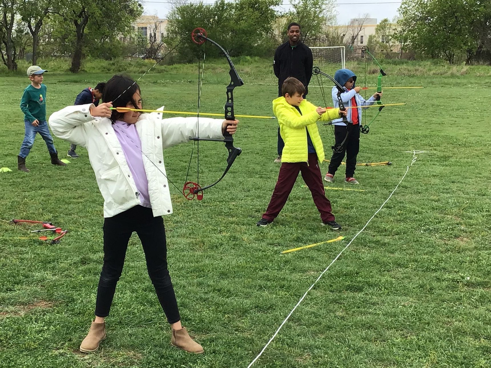 A Montessori group of children are practicing archery in a field