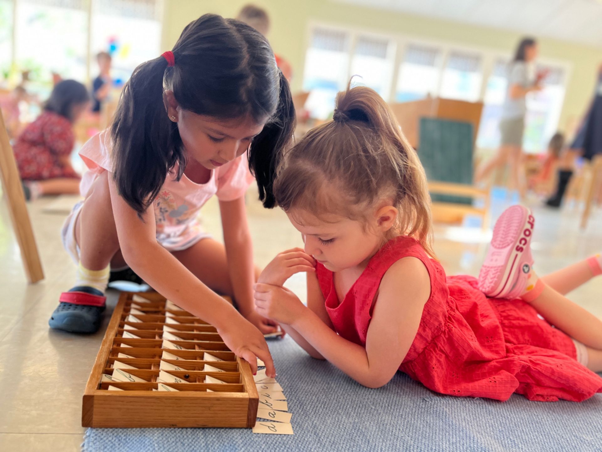 Two Montessori little girls are playing with a wooden box with letters on it
