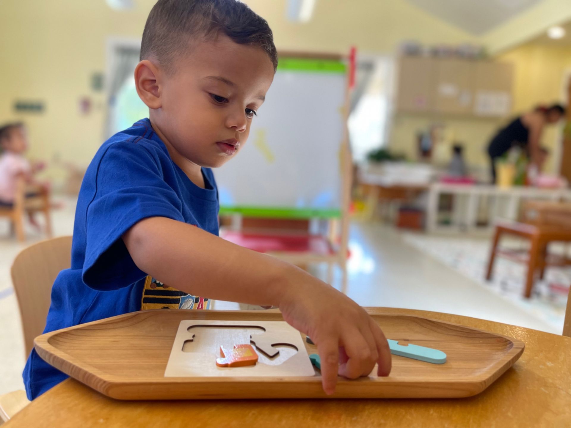 A Montessori child in a blue shirt is playing with a wooden tray