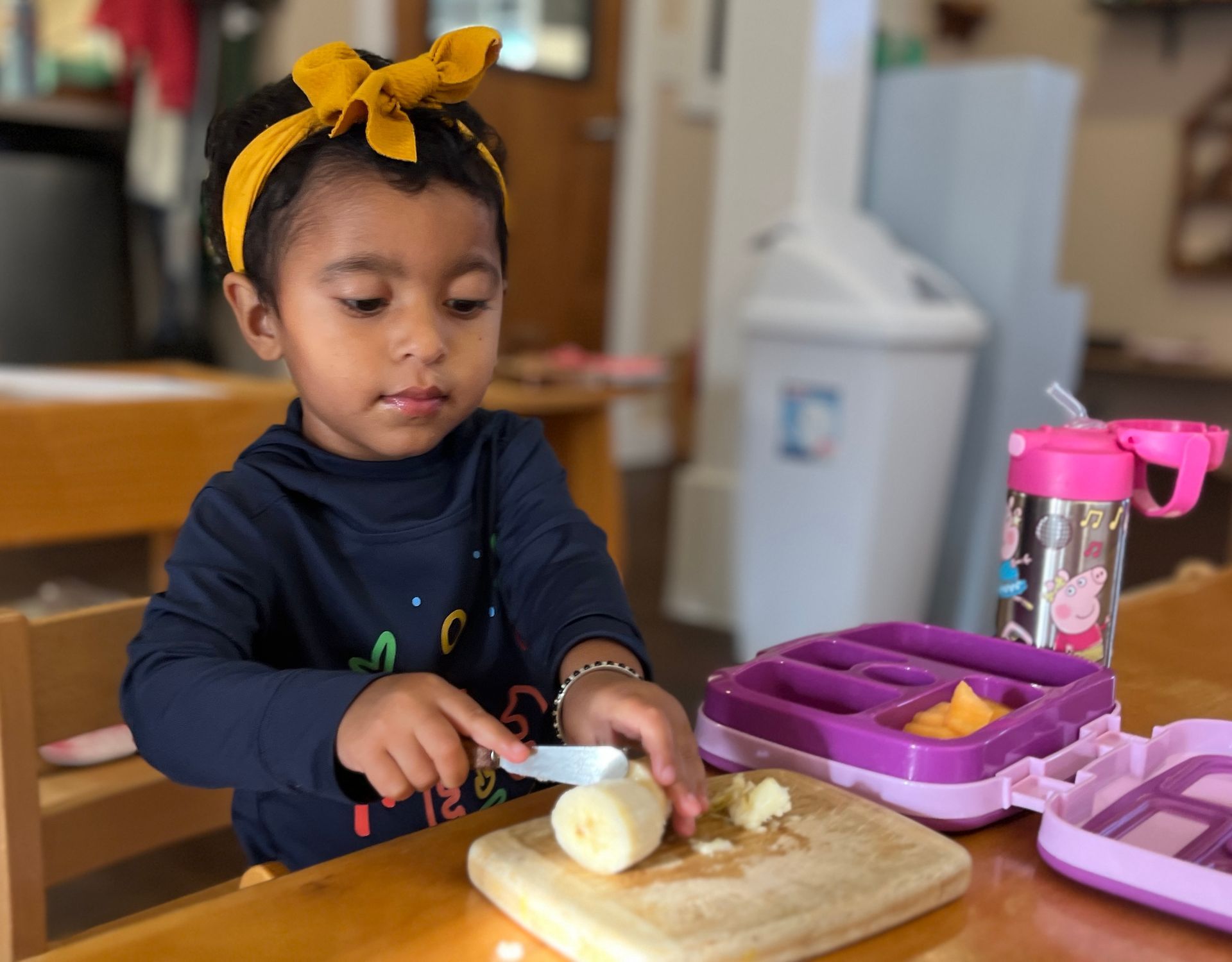 A Montessori  little girl is cutting a banana on a cutting board