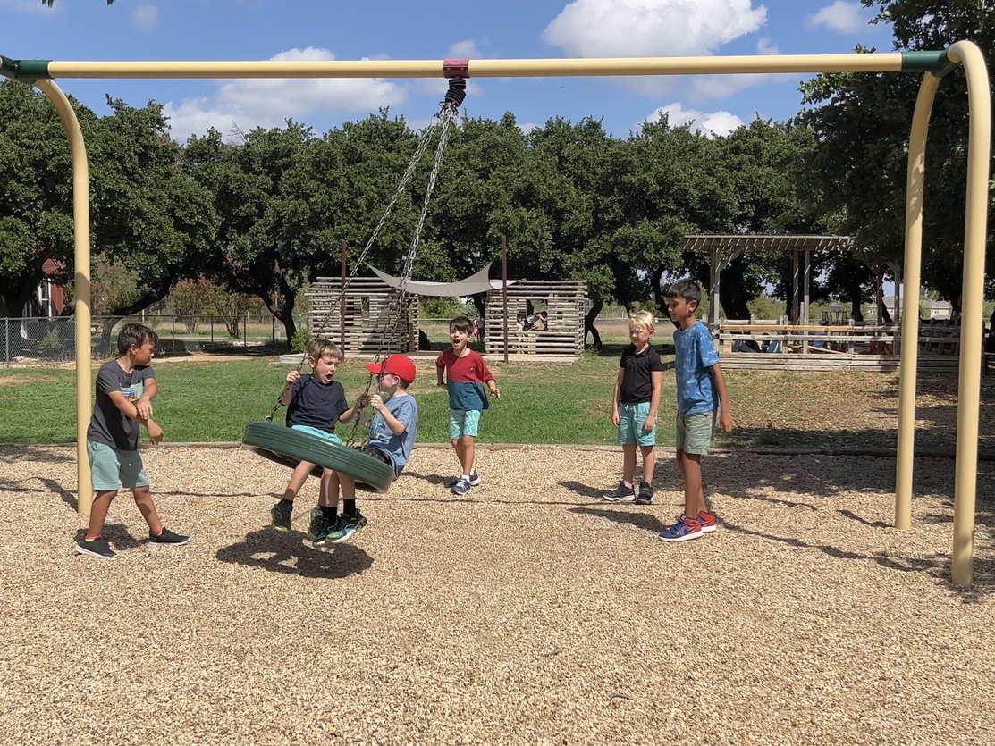 A Montessori group of kids are playing on a tire swing