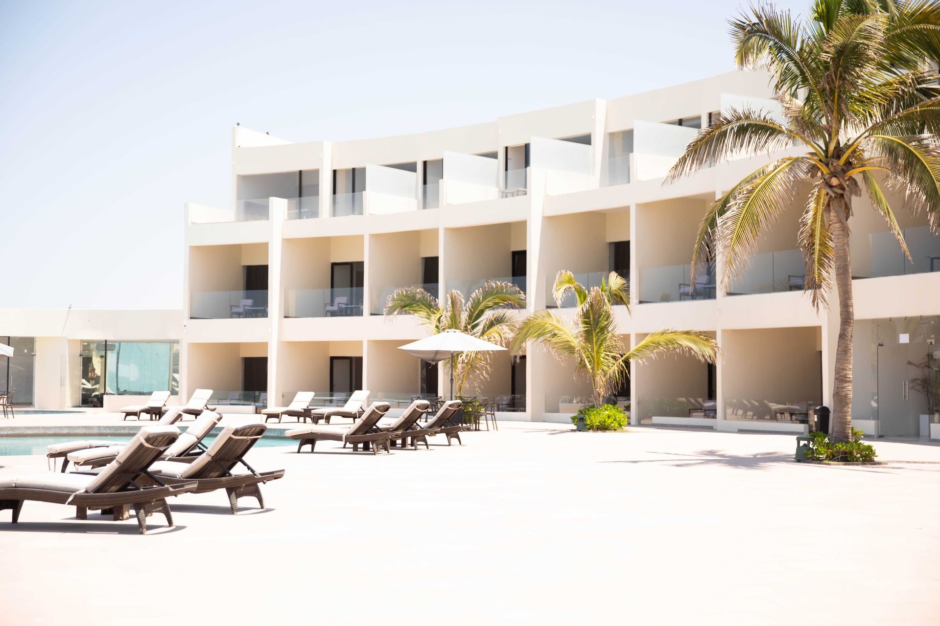 A large white building with a pool and chairs in front of it.