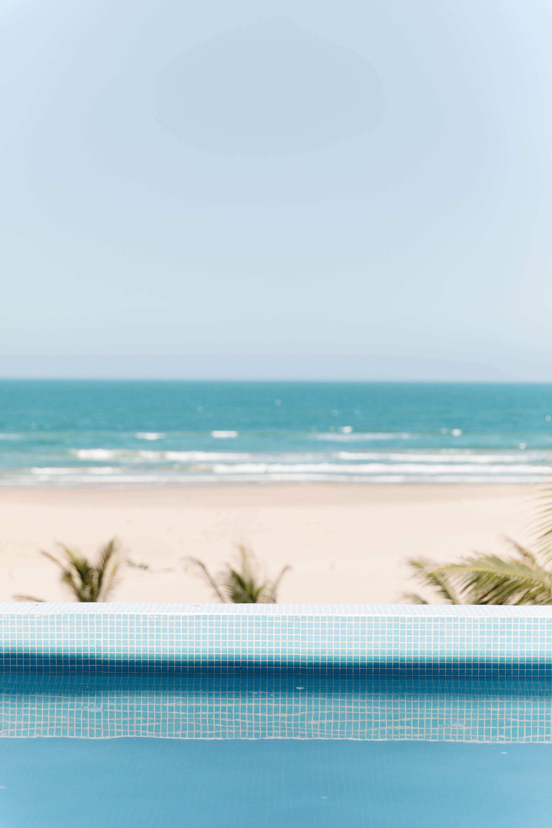 There is a swimming pool in the foreground and a beach in the background.