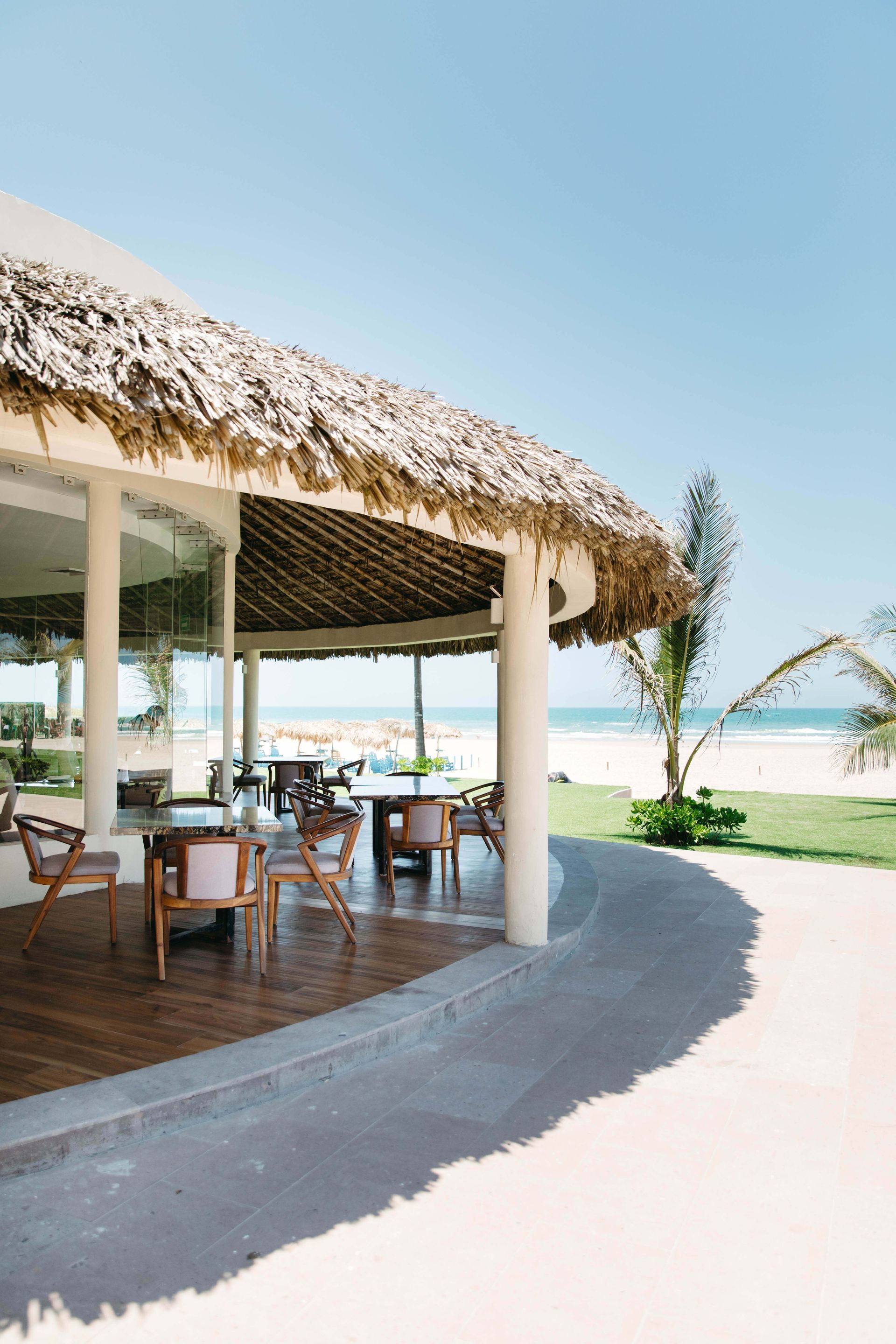 A restaurant with tables and chairs under a thatched roof.